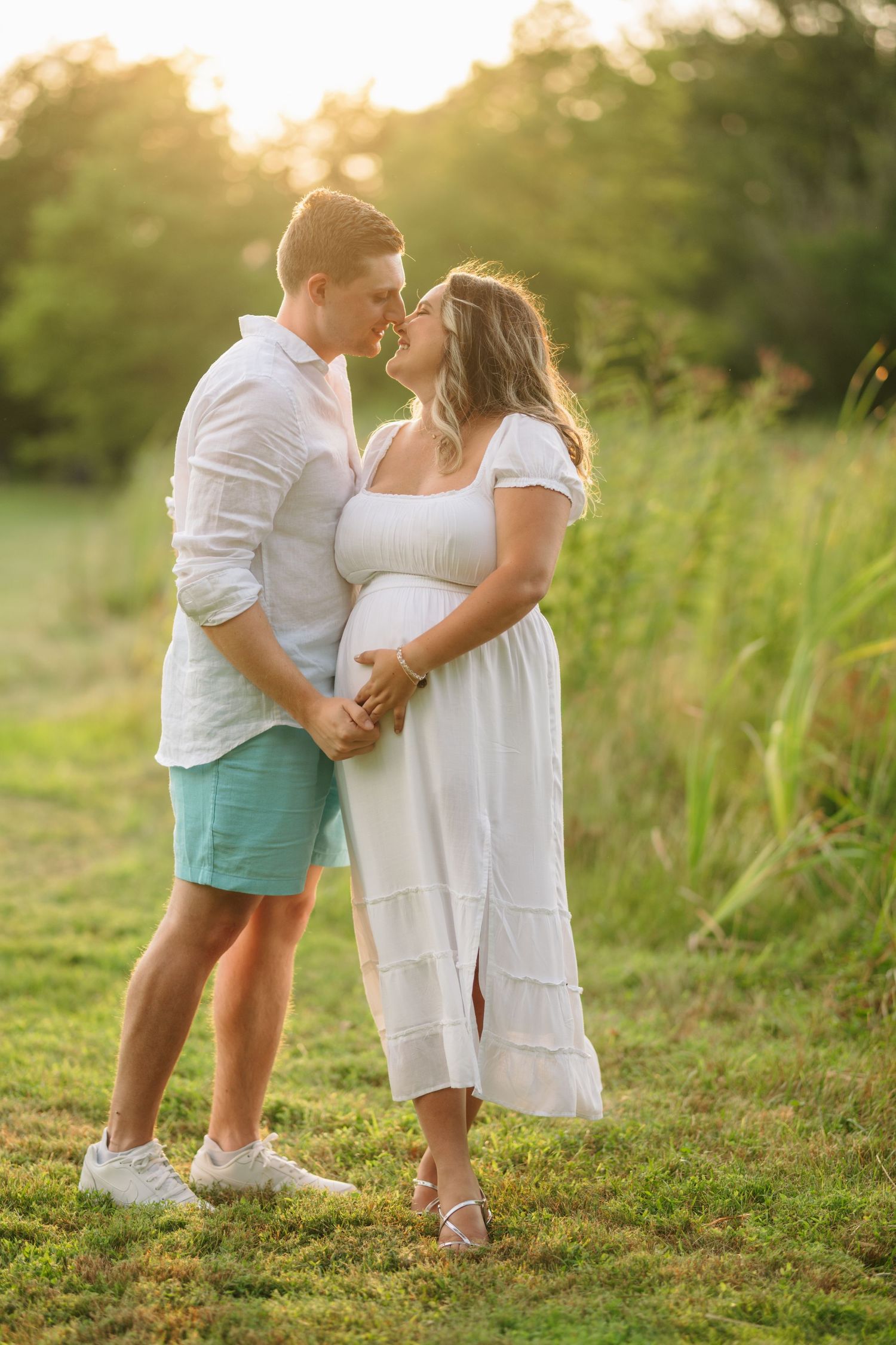 Maternity photoshoot captures romantic moment between couple in natural outdoor setting at sunset.