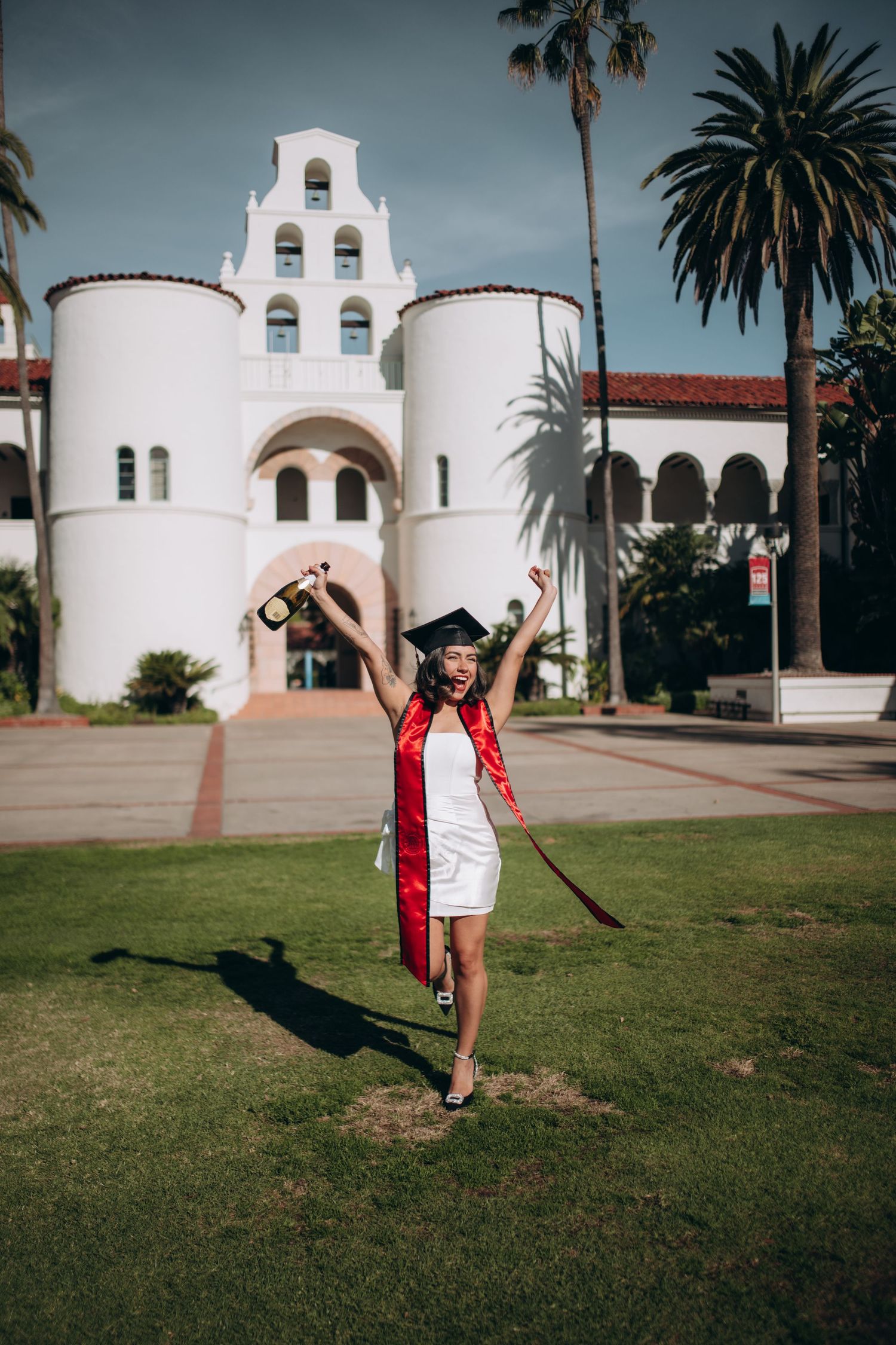 Graduate celebrates in front of Spanish mission-style university building with white towers.