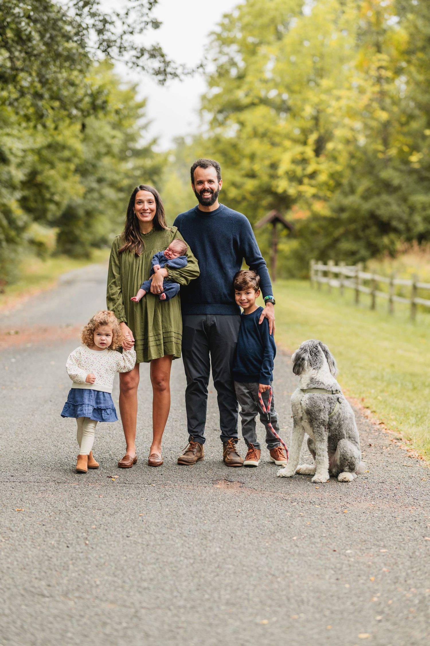 Family and their dog pose for portrait on autumn path with fall foliage.