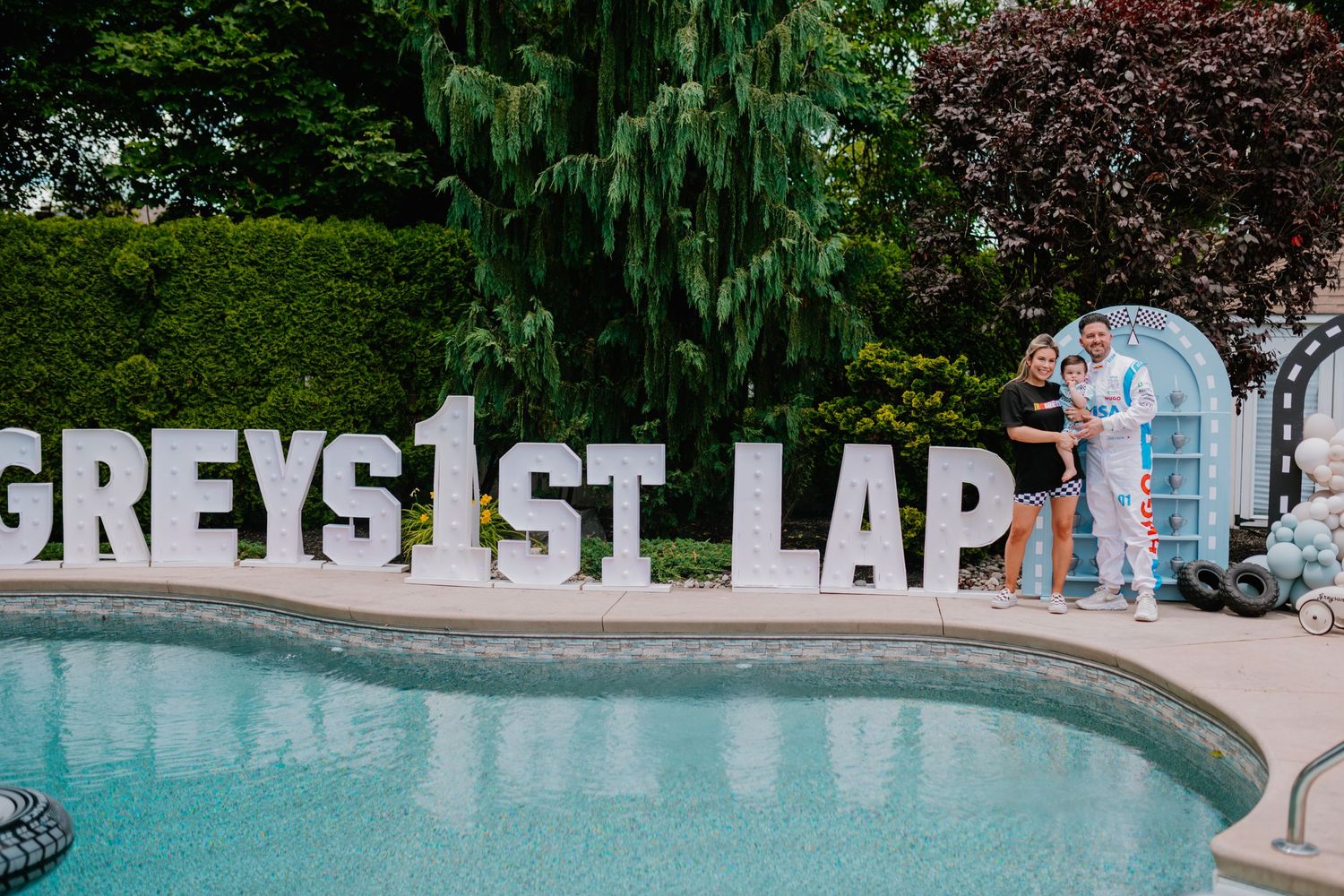 Large white letters spelling 'Greys 1st Lap' displayed beside swimming pool with blue accents.