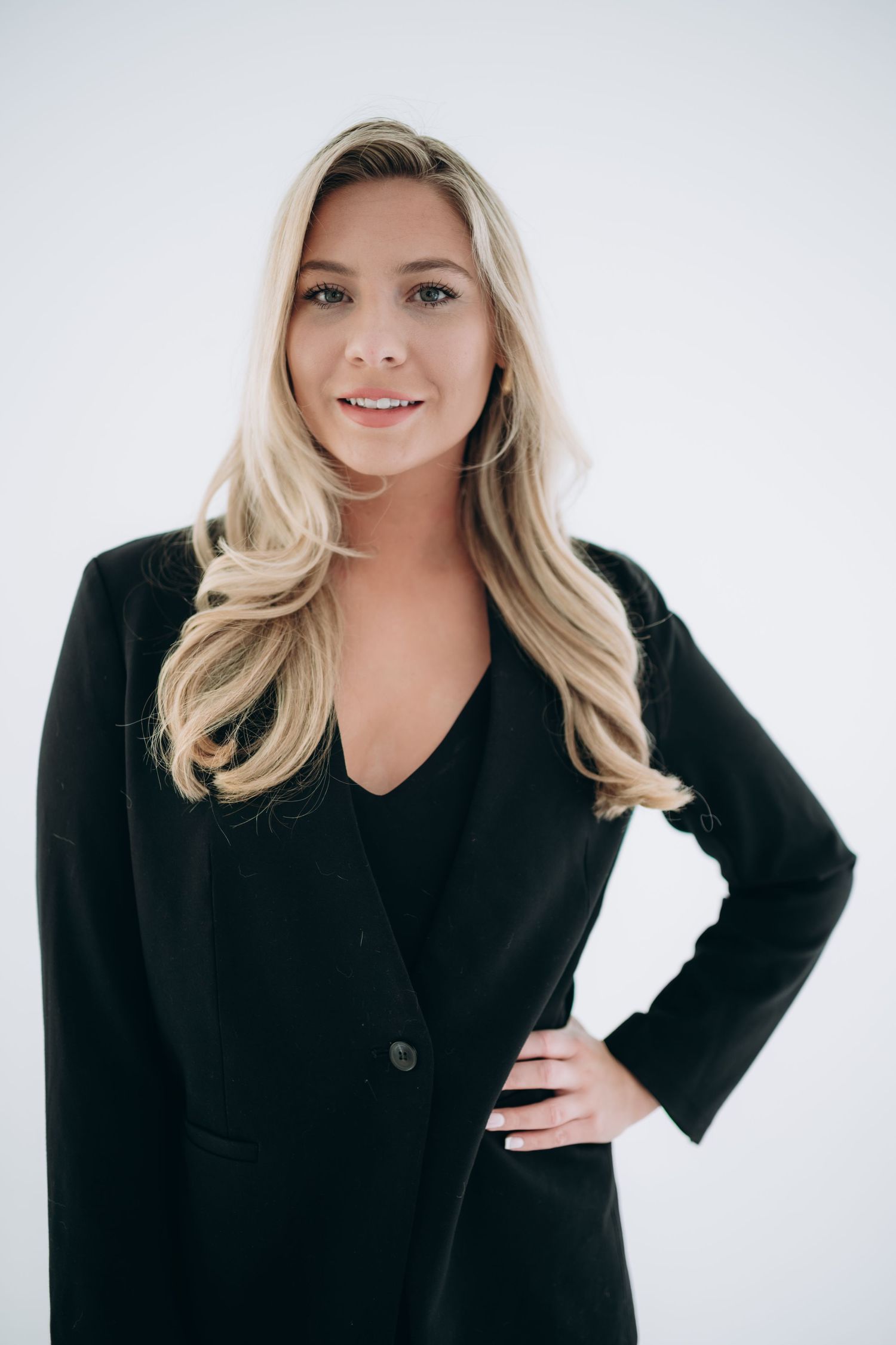 Studio portrait in black blazer with styled blonde hair against light background.