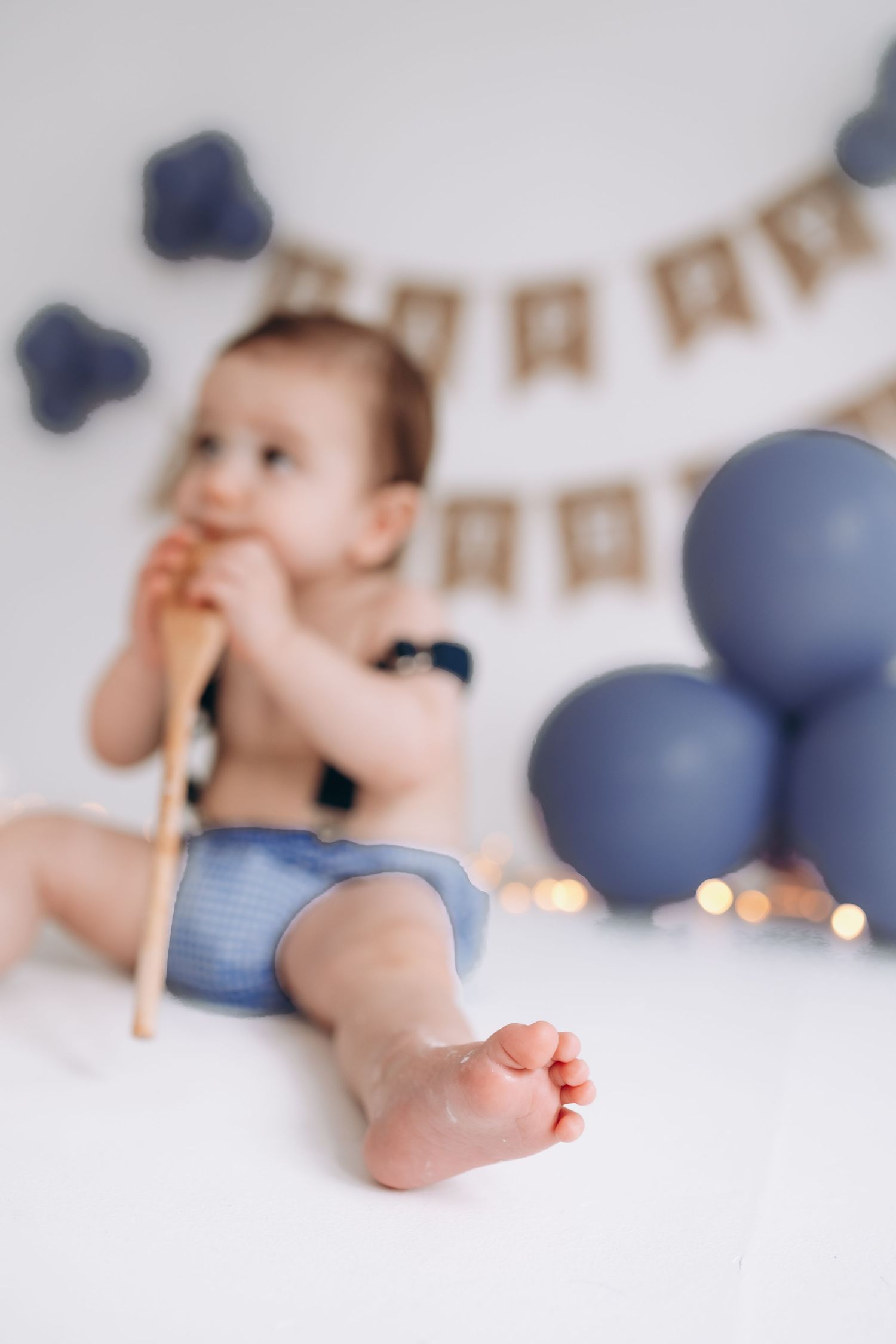 Birthday party setup with blue balloons and banner showing small bare feet on white backdrop.
