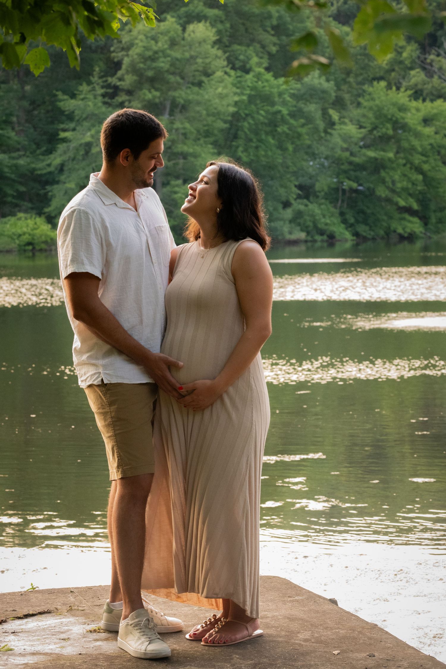 Couple shares an intimate moment by a serene lake during a maternity photoshoot in nature.