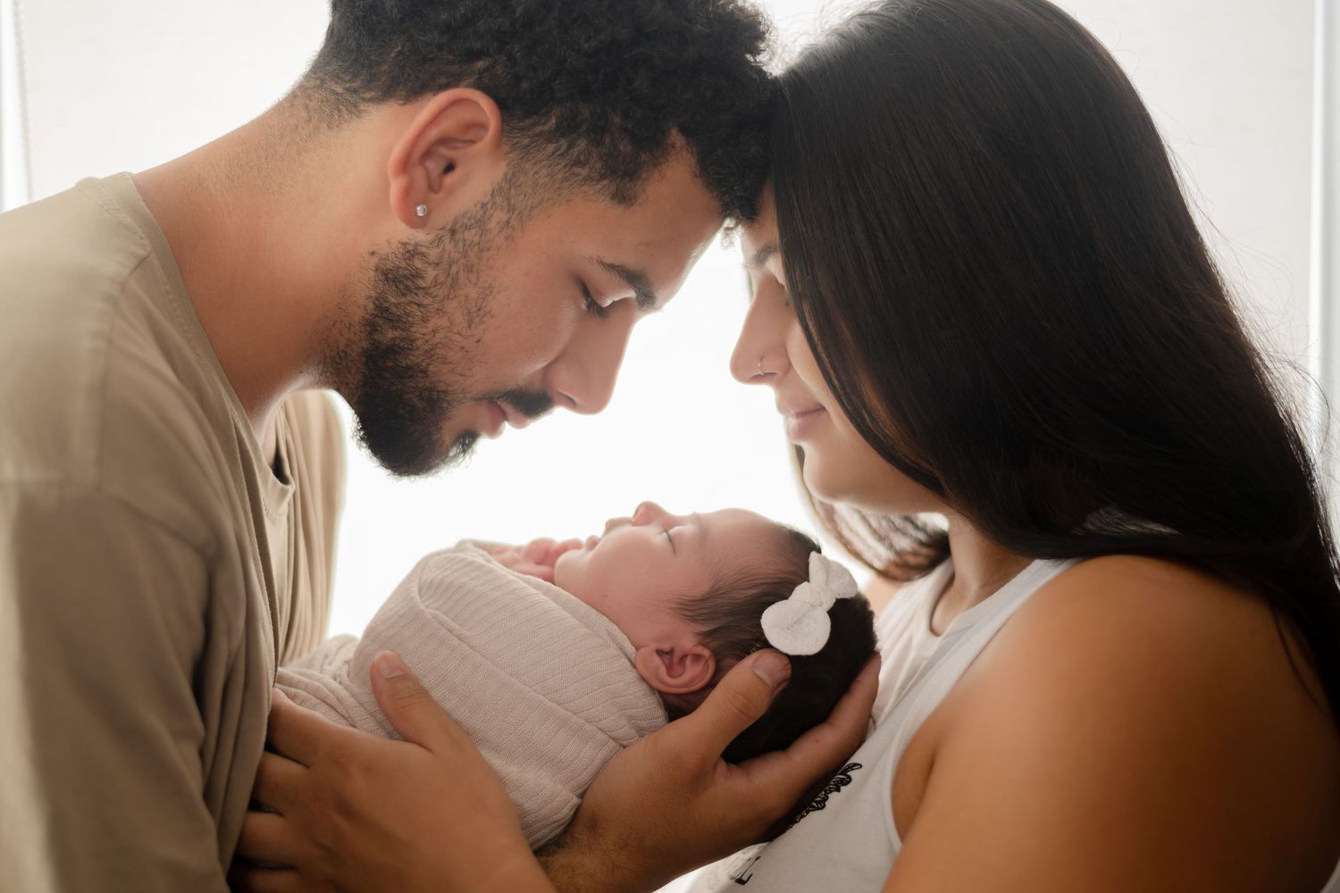 Parents sharing intimate moment with newborn baby against white background.