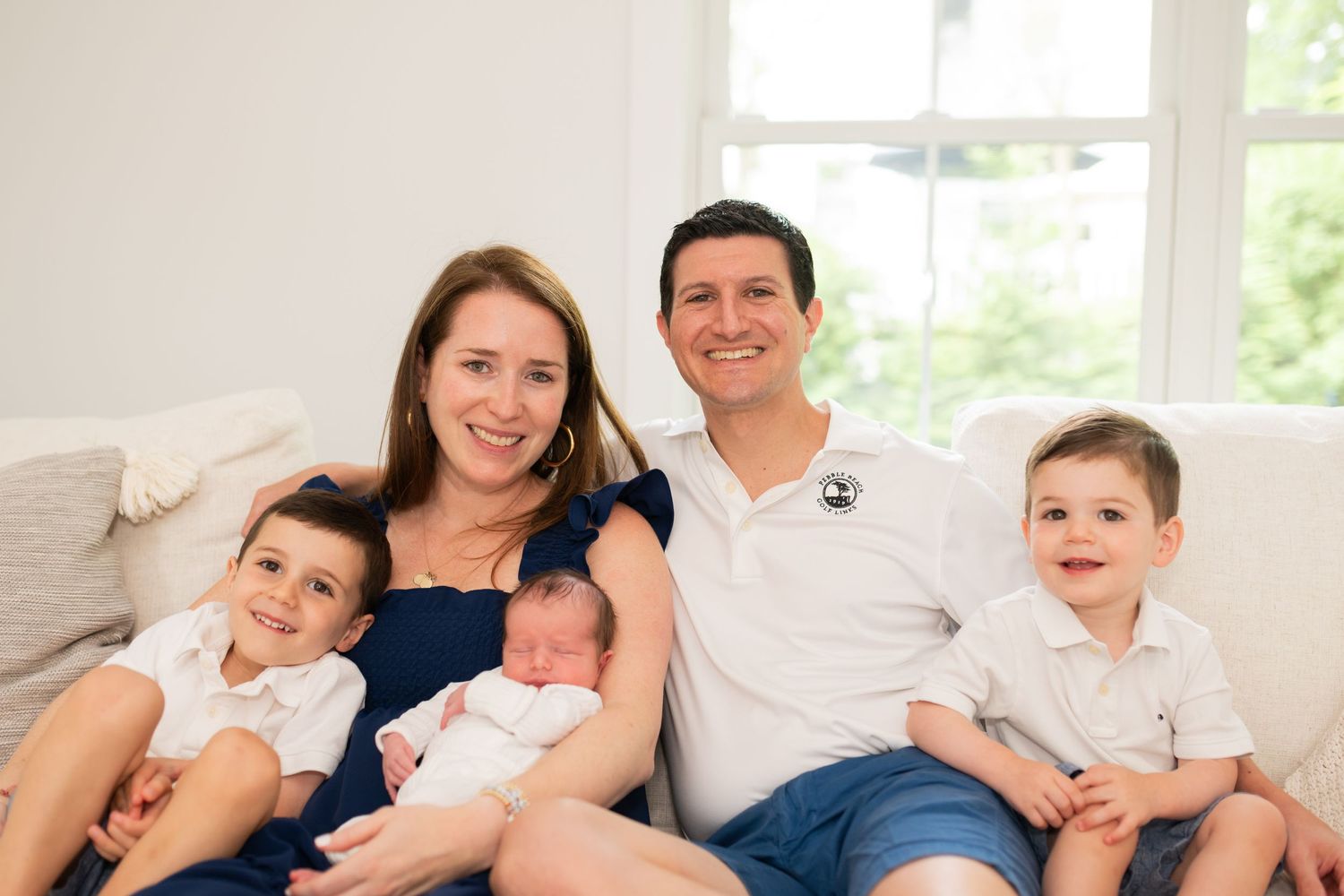 Happy family of five posing together on white couch for portrait.