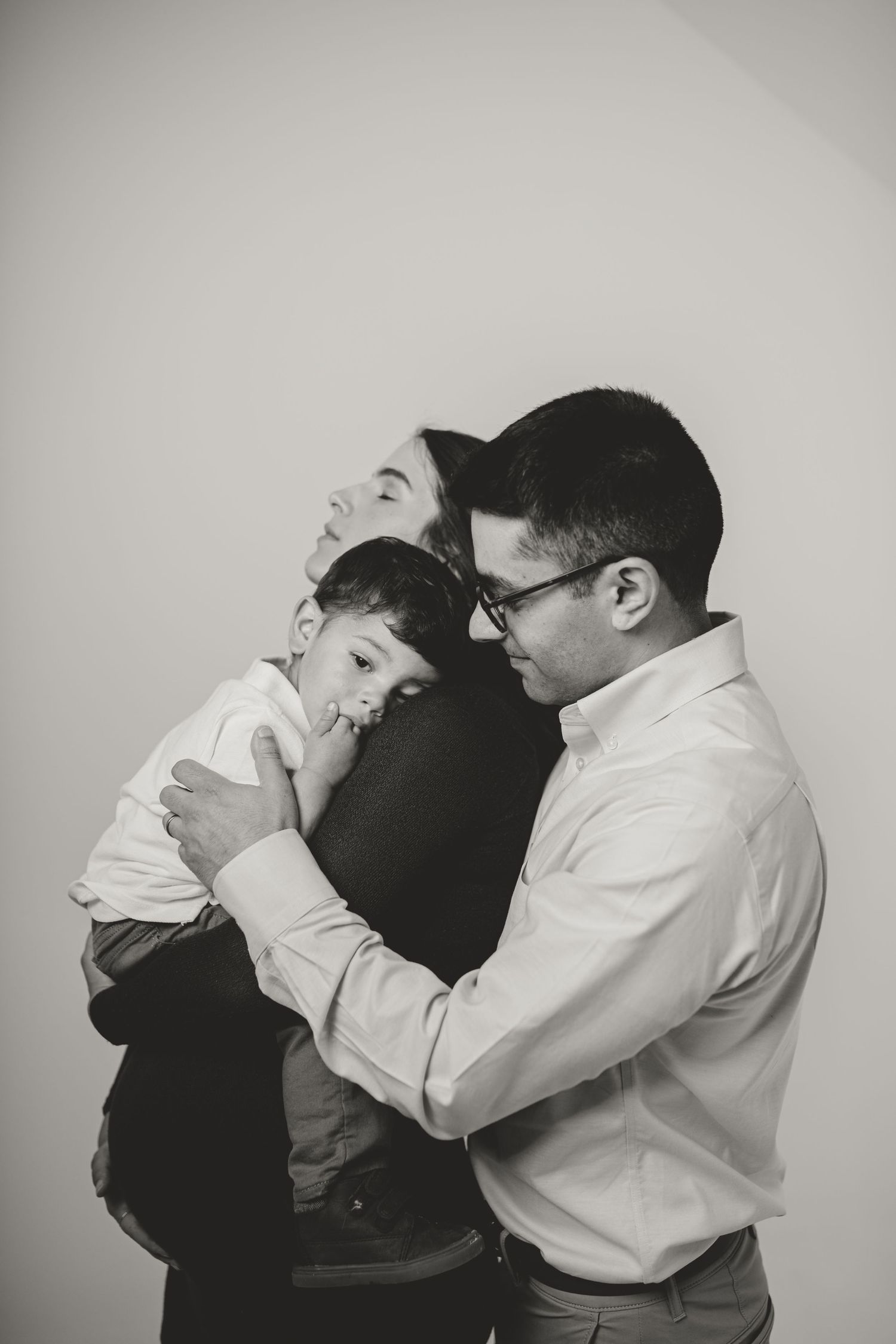 Black and white intimate family portrait against neutral background.
