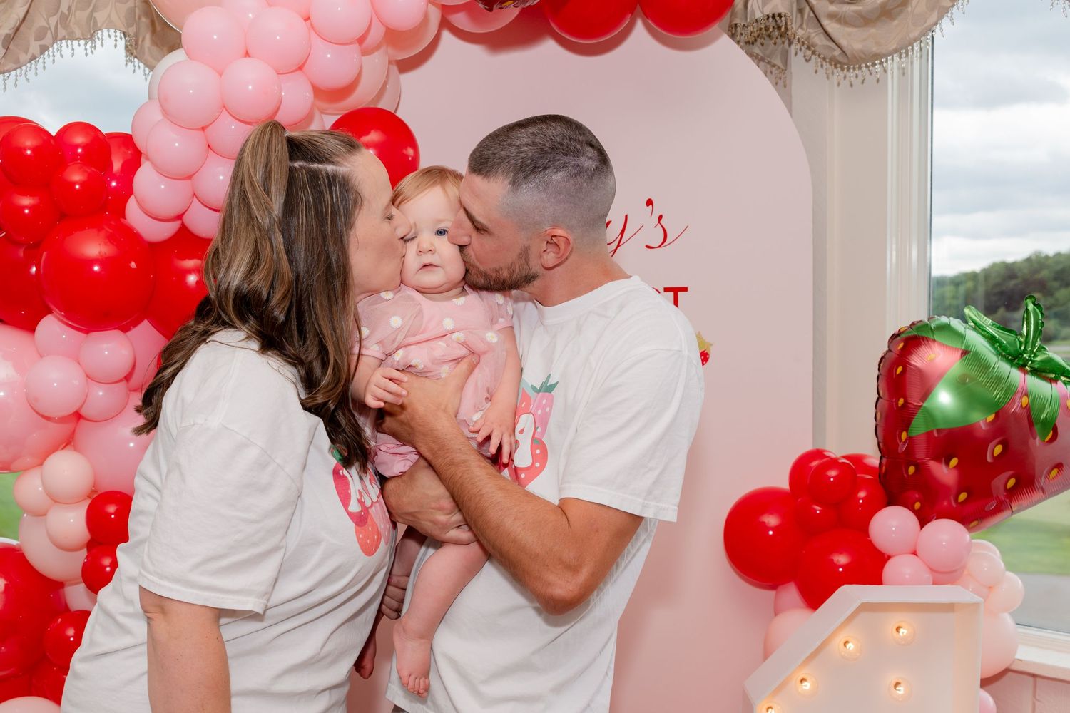 Baby celebration with pink and red balloon arch decorations and festive party atmosphere.