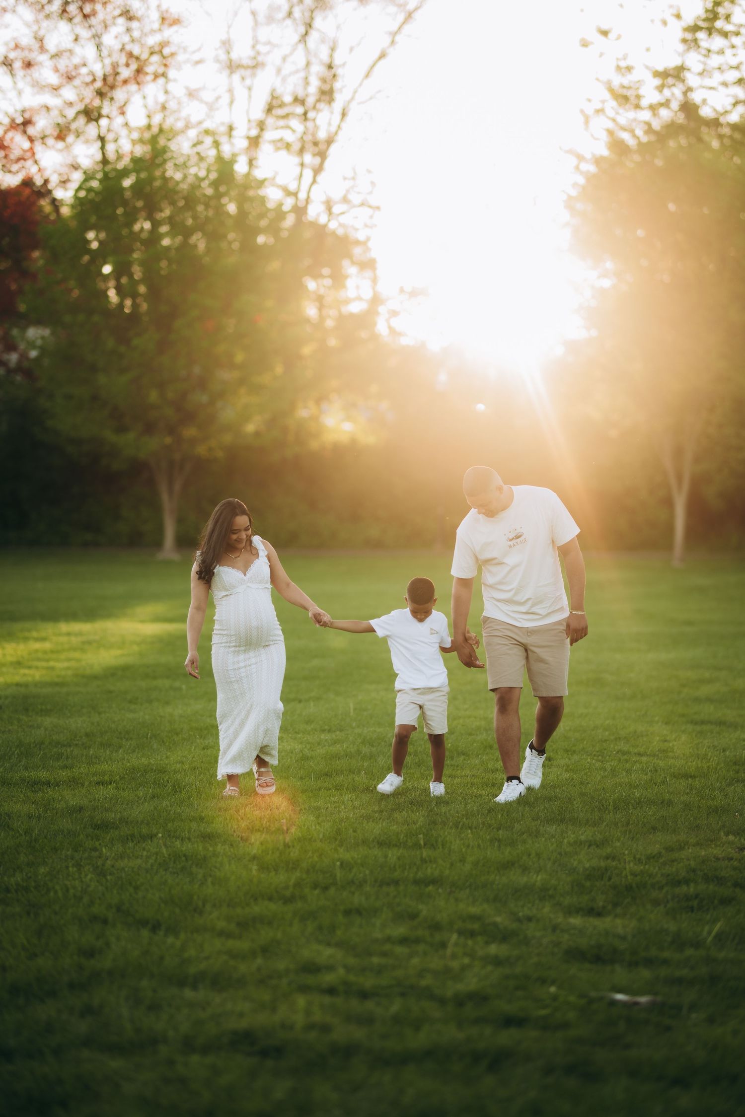 A family walks hand in hand through a grassy field at sunset with golden sunlight streaming through trees.