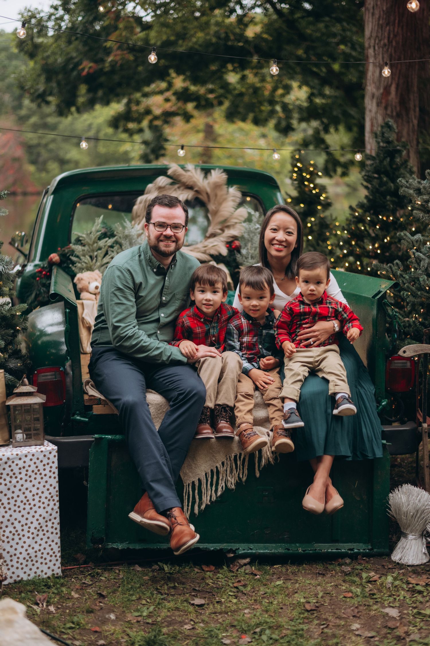 Family poses together on vintage green truck with Christmas lights and decorations.
