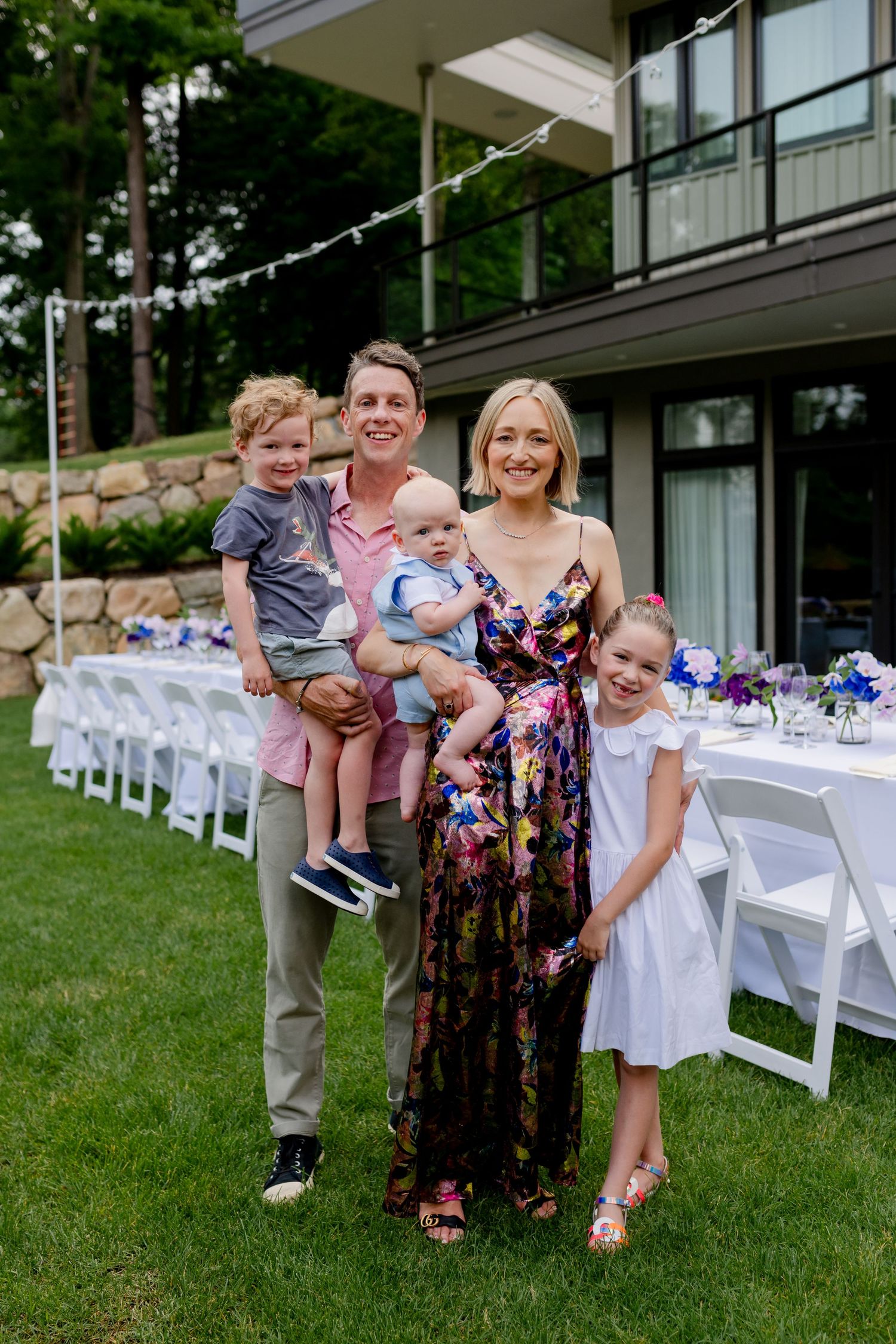 Outdoor celebration with family standing by decorated white tables on lawn.