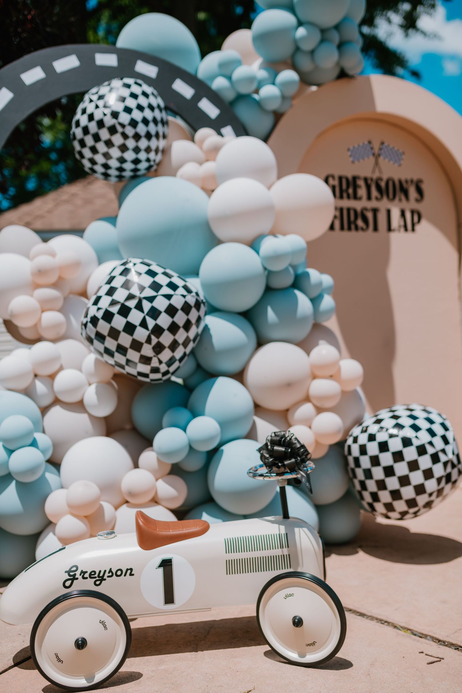 Vintage race car themed first birthday party decoration with blue and white balloon arch.