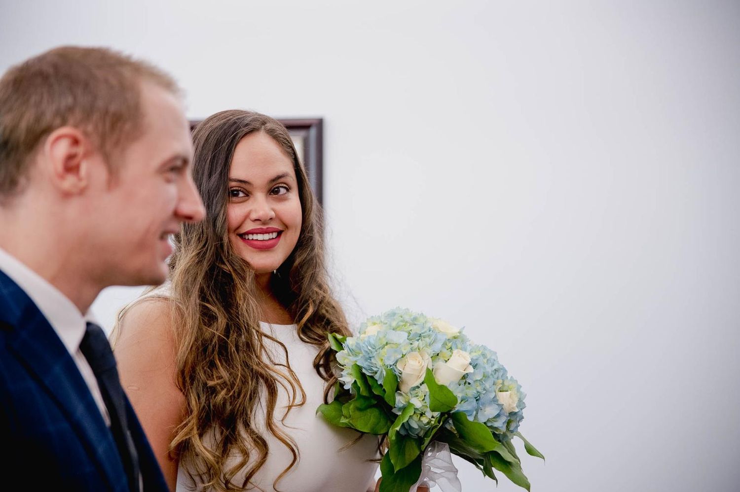 A wedding couple sharing a joyful moment while holding a bouquet indoors.