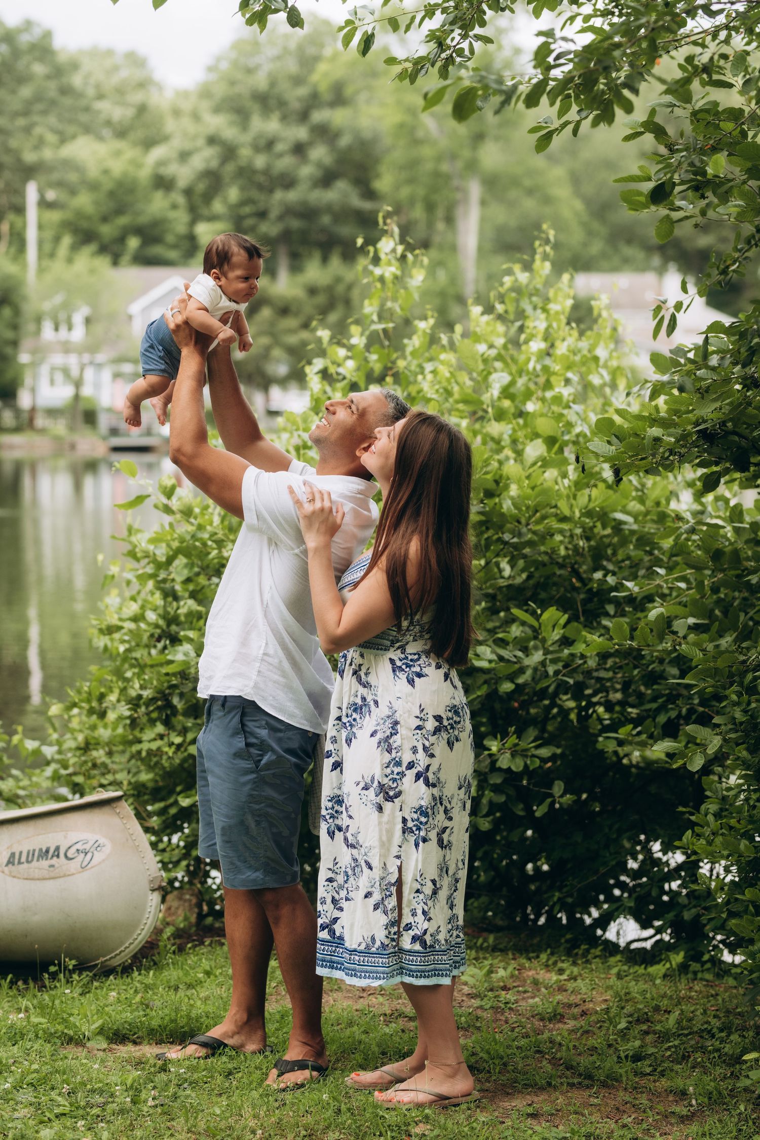 Two people share a joyful moment while standing near green foliage and a lake on a summer afternoon.
