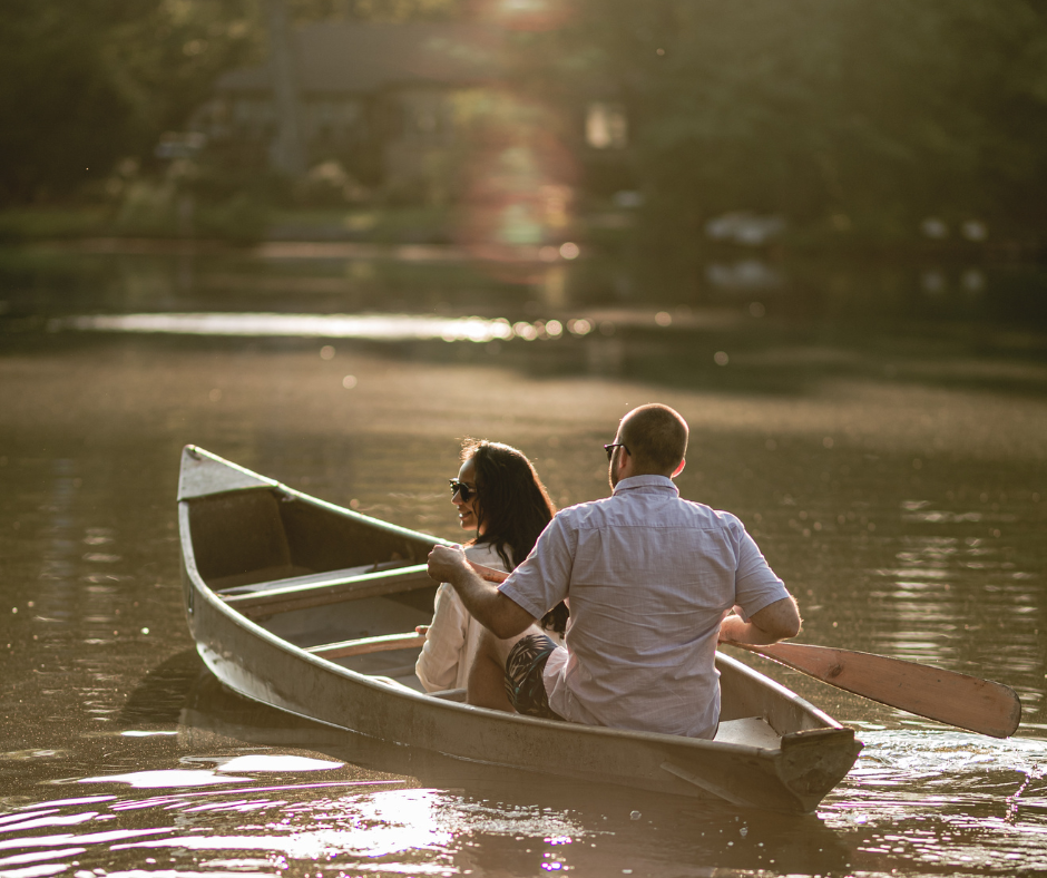 Two people paddle together in a canoe on a peaceful lake during golden hour as sunlight filters through the trees.