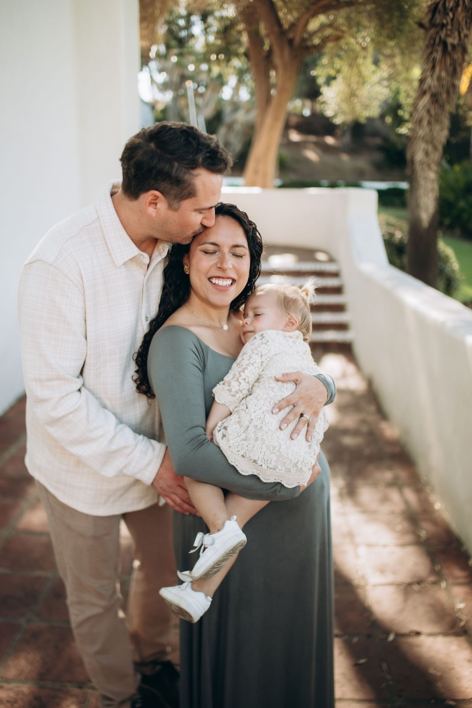 Intimate family moment captured outdoors with sunlight filtering through trees.