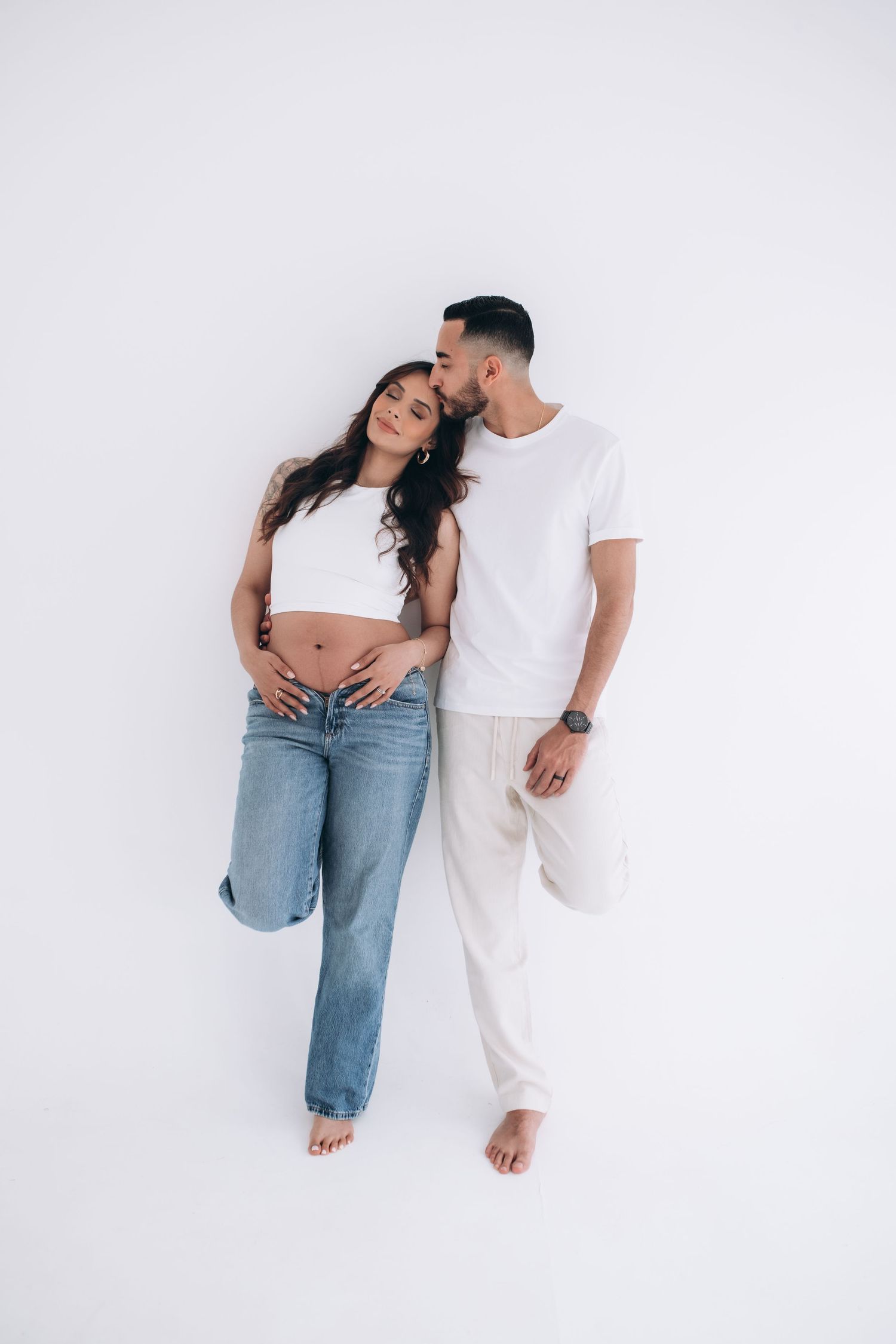 A couple in casual white and denim outfits embrace against a white background.