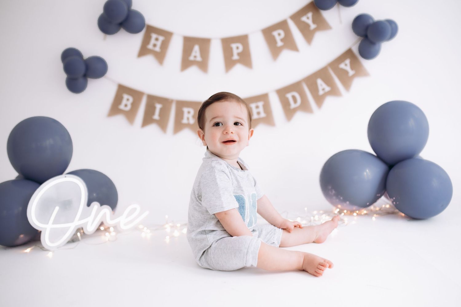 First birthday party setup with navy blue balloons and kraft paper banner against white backdrop.