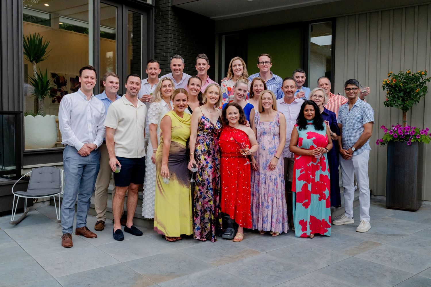 Large group photo of people in summer attire gathered outside modern building.