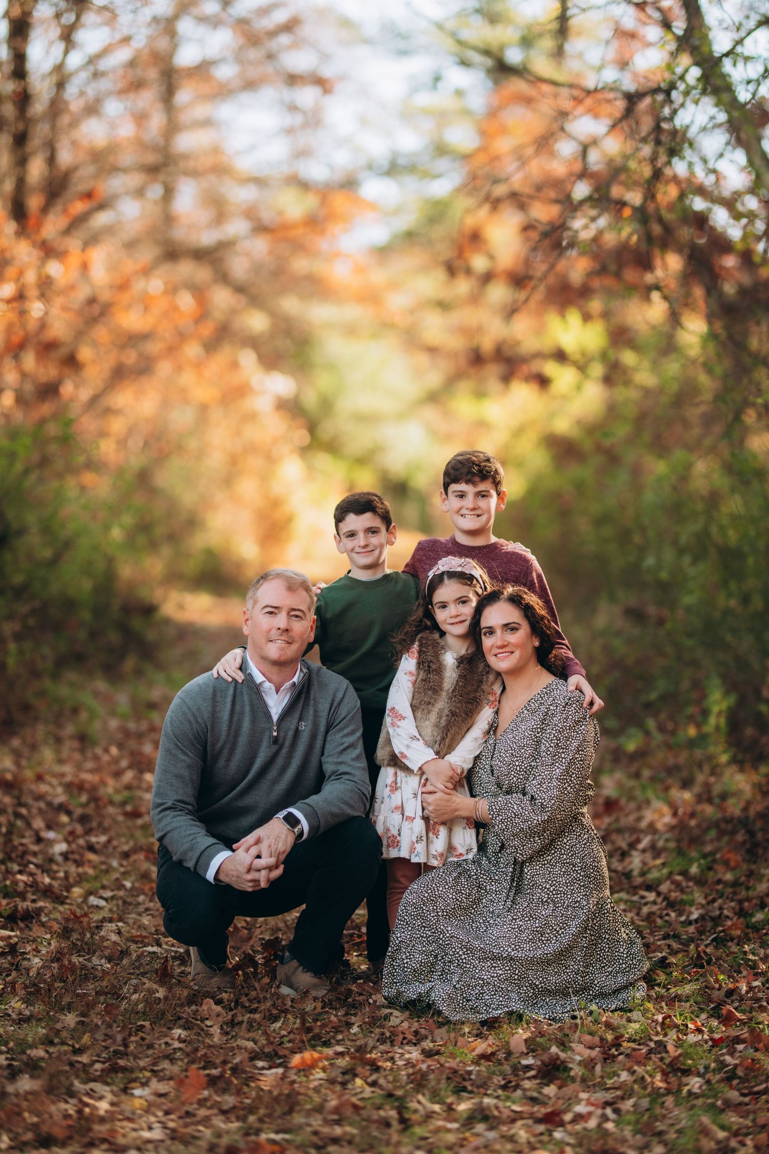 Family portrait captured outdoors during autumn with fall foliage in the background.