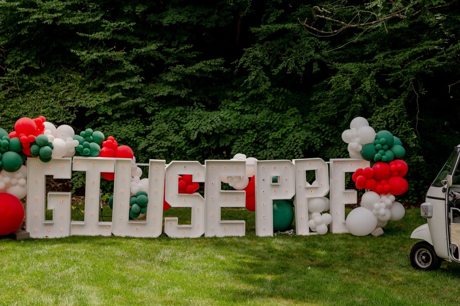 Large white letter decorations spelling 'Giuseppe' with red, white and green balloon garland.