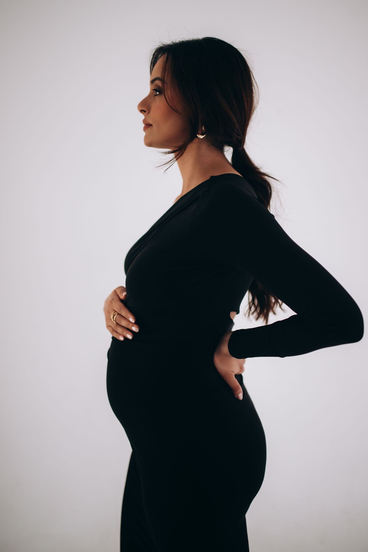 Side profile silhouette of an expectant mother in a fitted black dress against a light background.