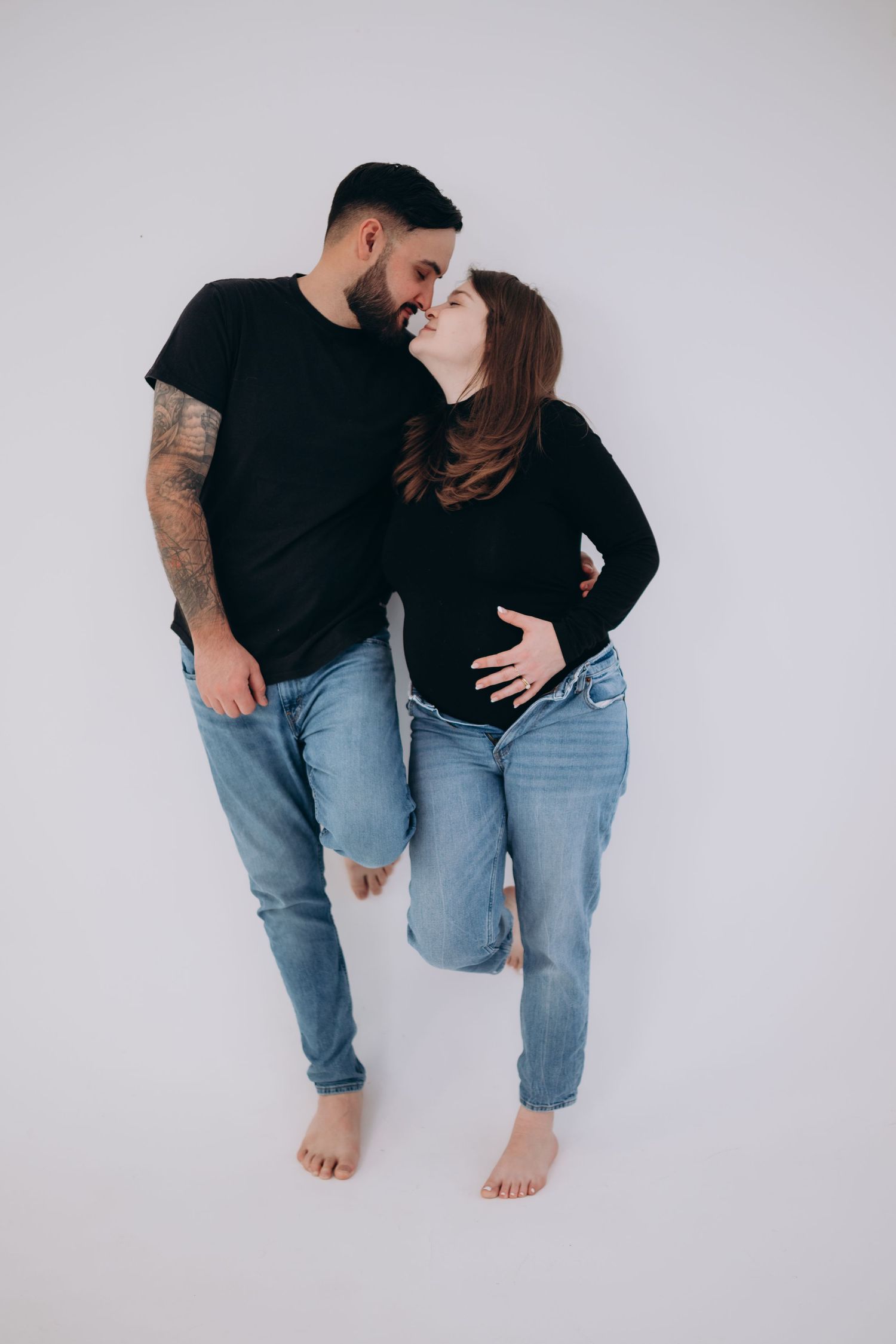 Playful couple in matching dark outfits pose against white backdrop in casual photoshoot.