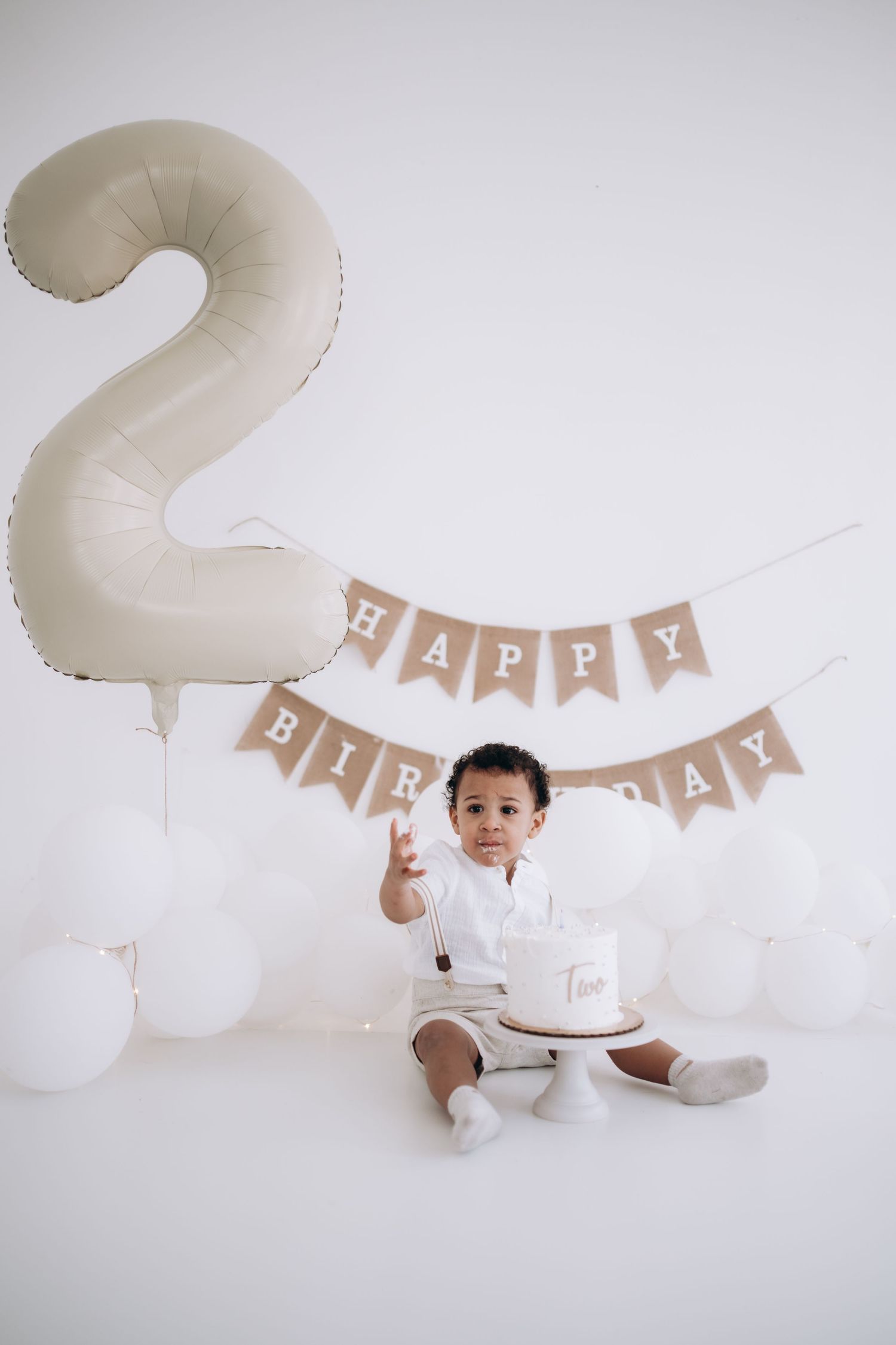 Birthday setup with large number 2 balloon, banner, and toddler with cake.