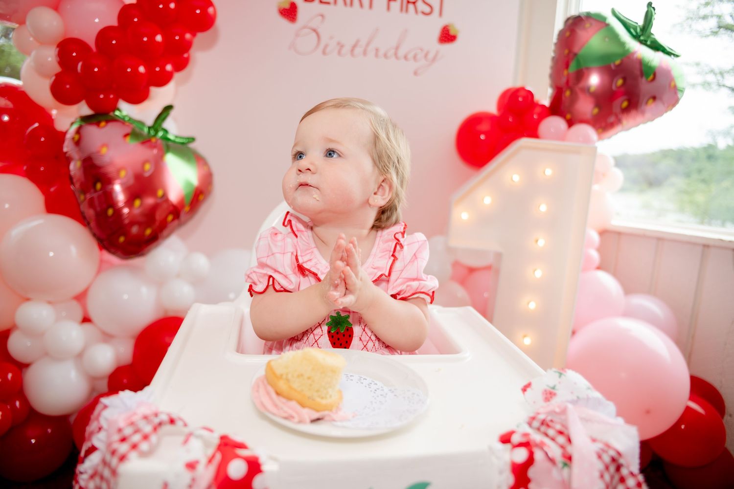 Little one enjoying their first birthday with strawberry themed decorations and pink balloons.