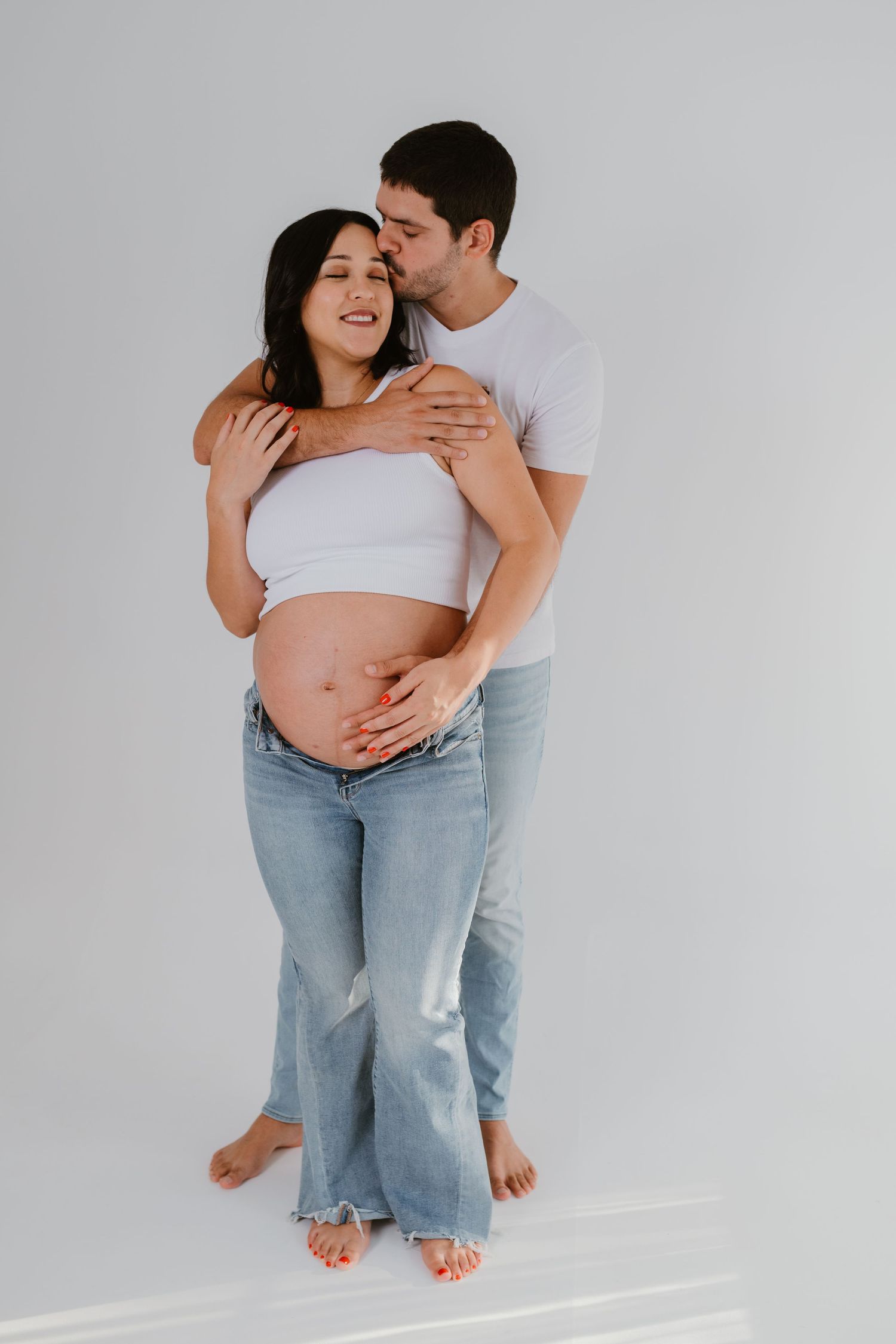 Intimate maternity portrait of couple embracing against white background.