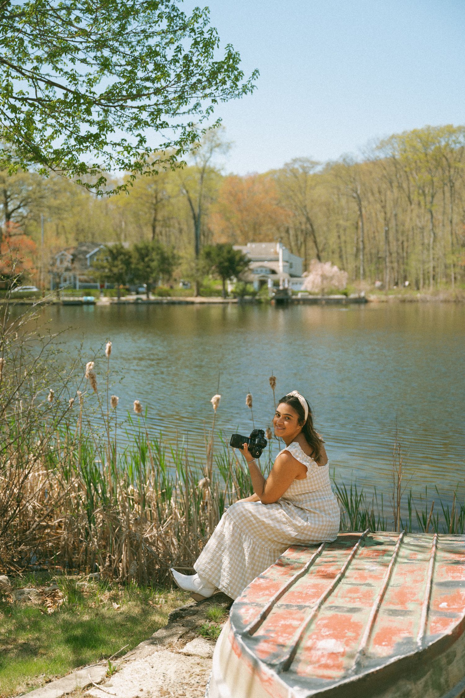 Photographer takes artistic photos on colorful blanket by peaceful lake surrounded by spring trees and water reeds.