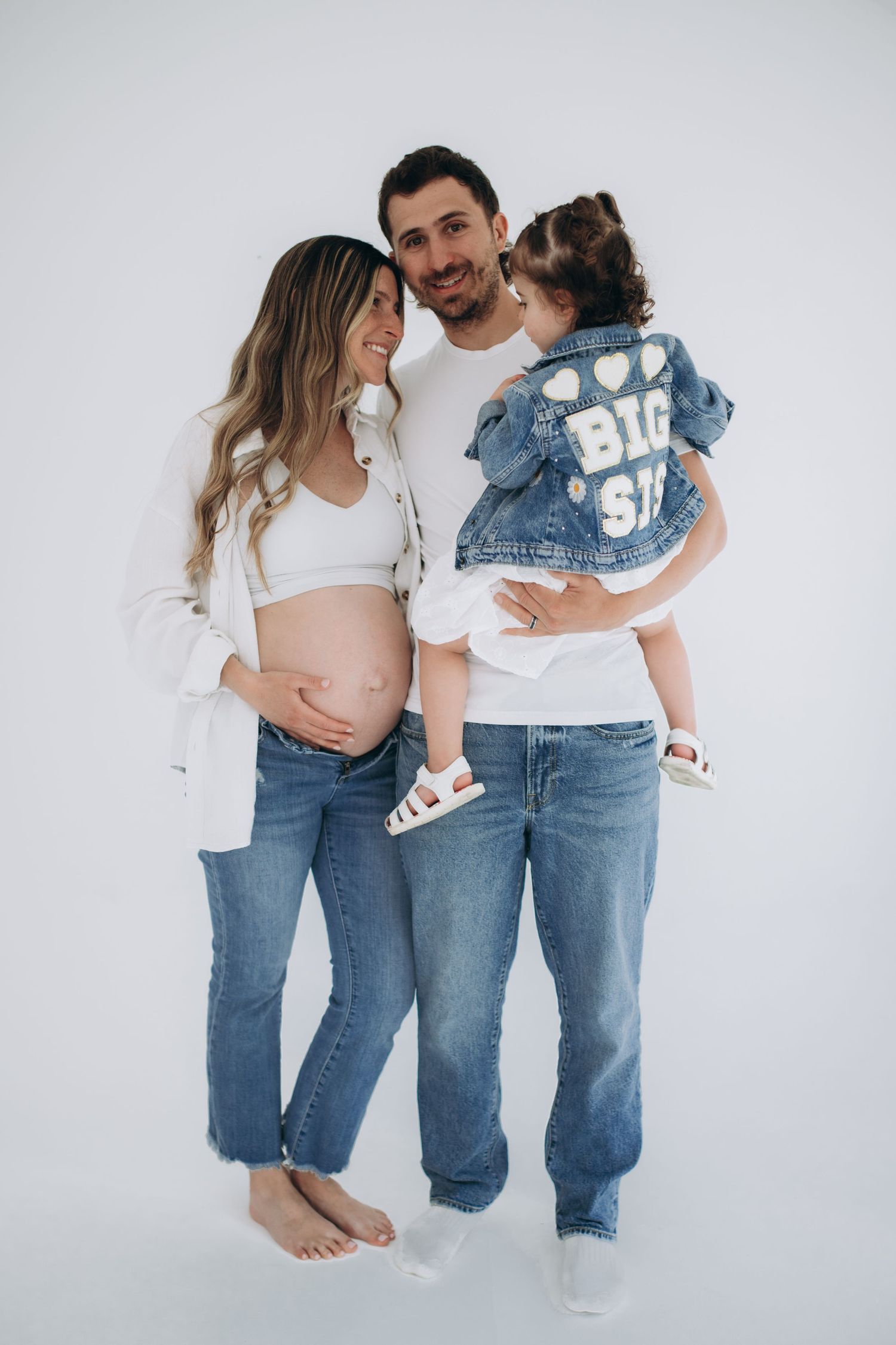A family wearing matching white shirts and blue jeans poses for a series of casual lifestyle photos against a white backdrop.