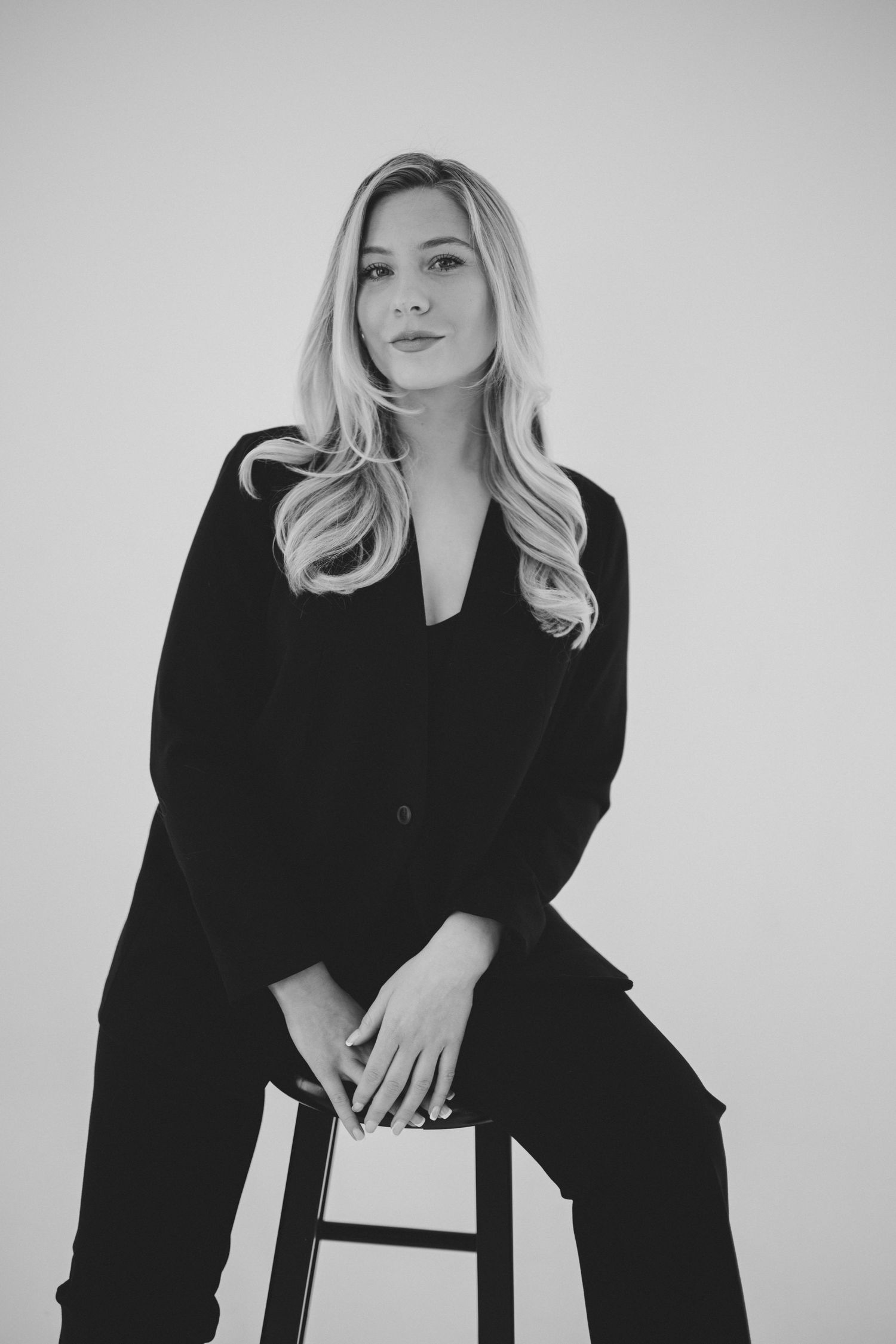Black and white portrait sitting on stool in professional attire.