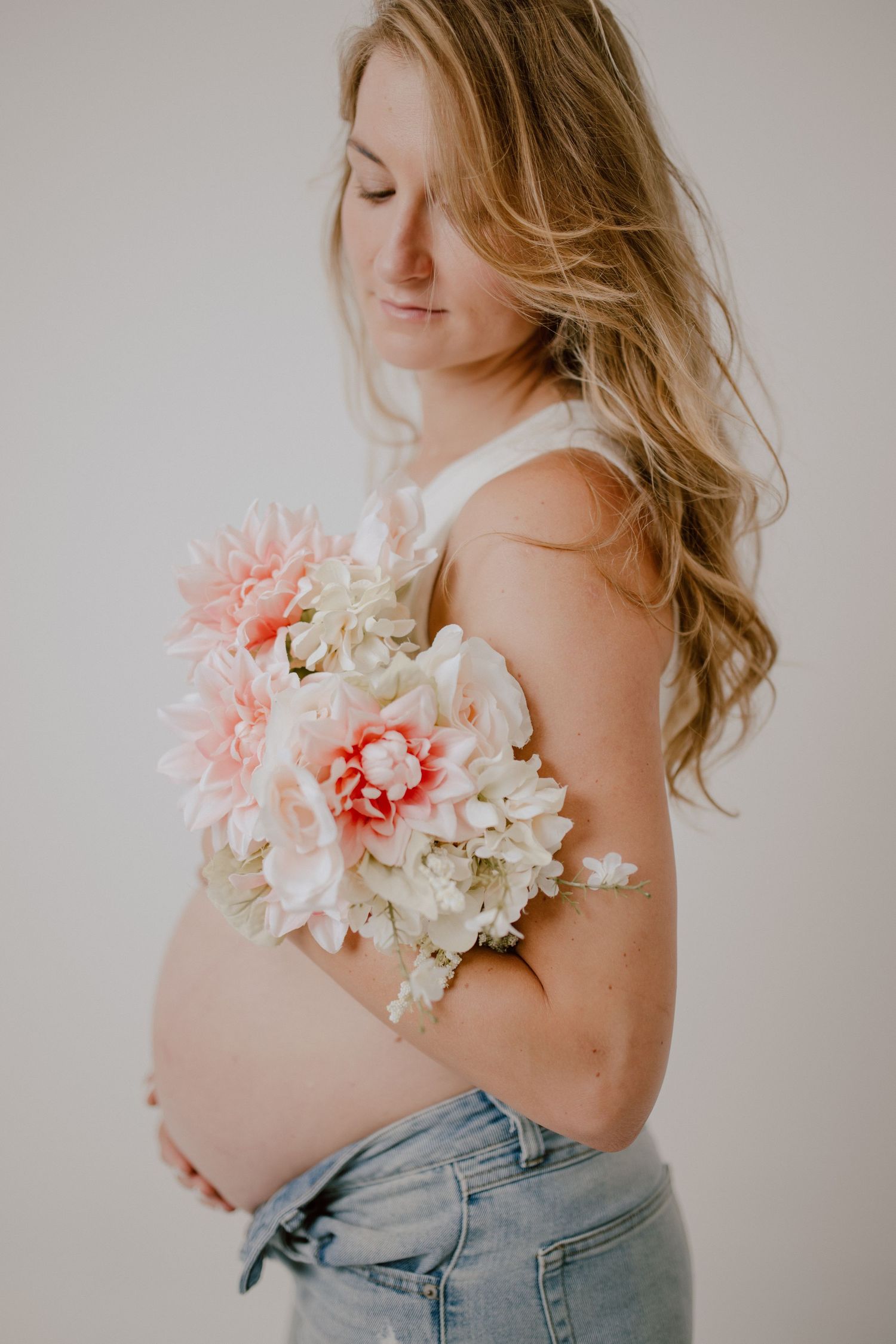 Maternity portrait featuring pink and white flowers against bare pregnant belly.