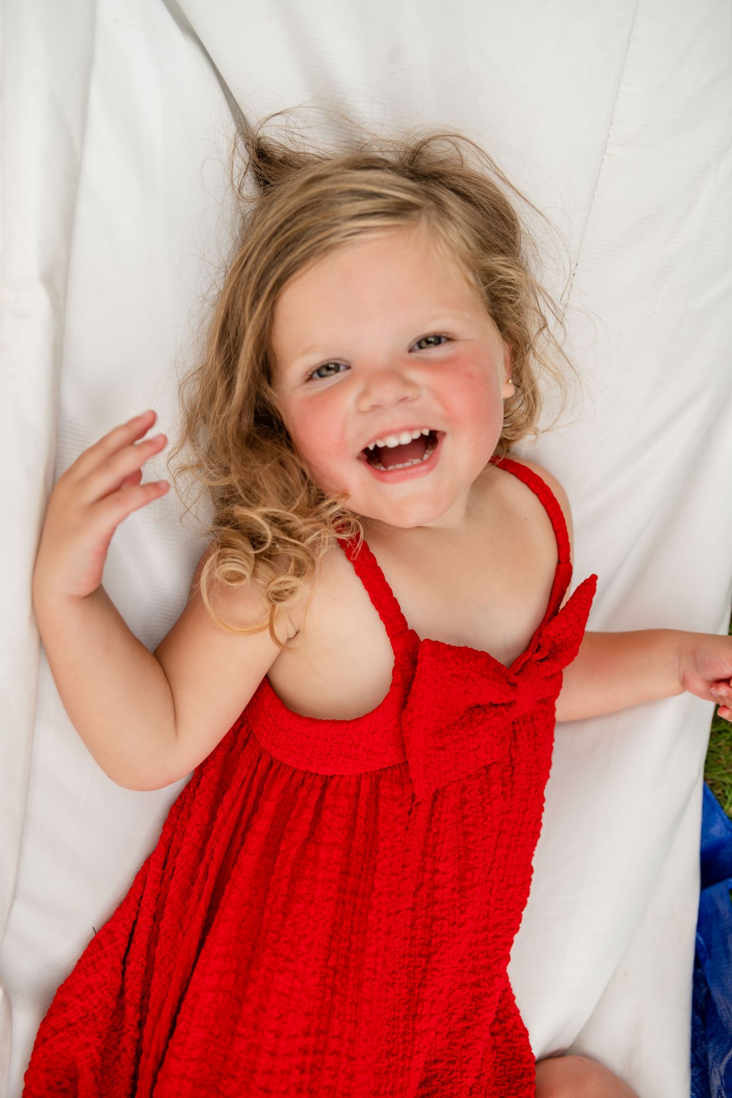 Cheerful child in red dress laughing while lying on white background.