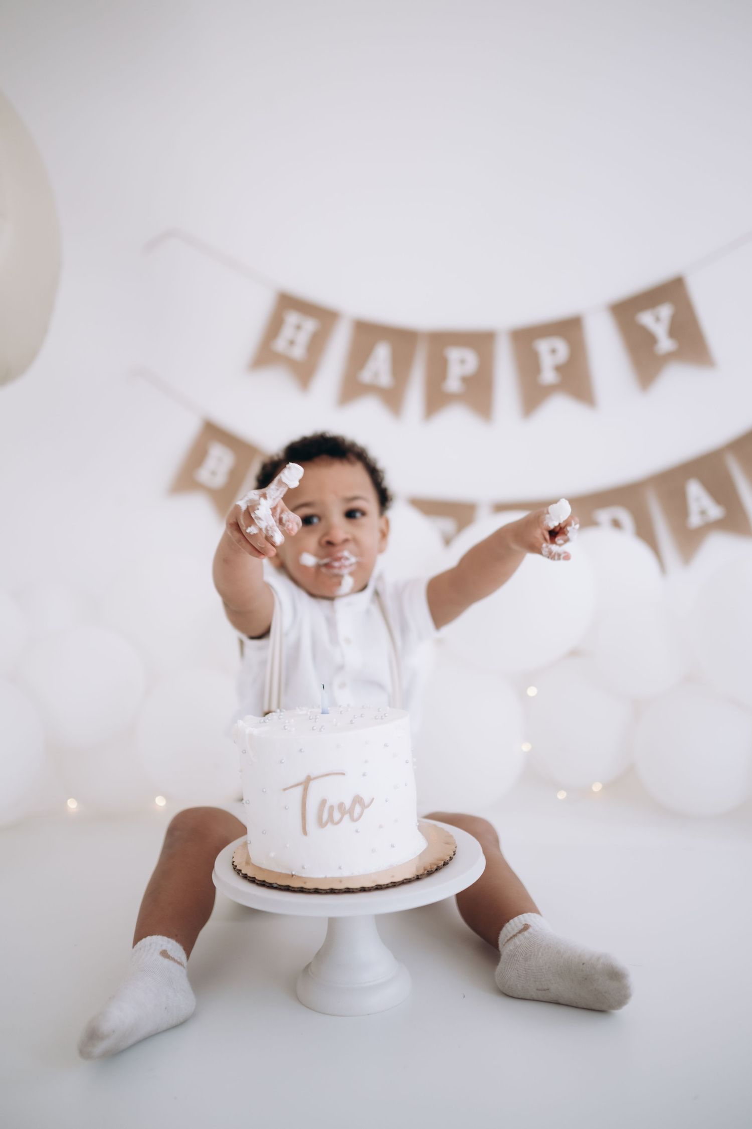 milestones session, Toddler reaching toward camera while sitting with birthday cake and decorations.
