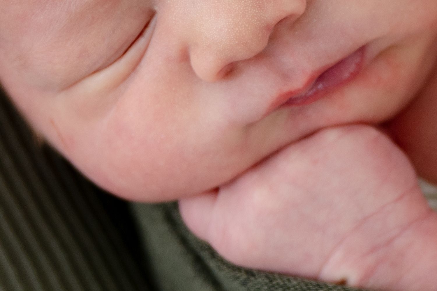 Close-up macro shot of a baby's soft pink cheek and lips resting against a dark green fabric.