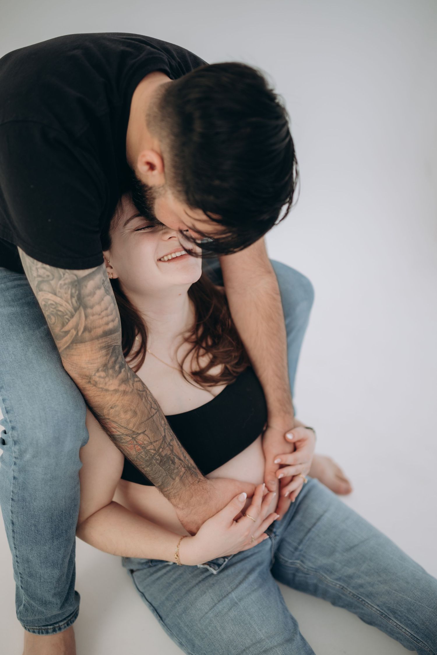 Intimate couple photoshoot featuring casual denim and black outfits against white background.