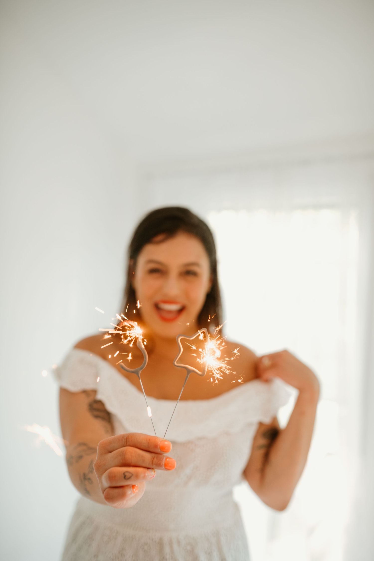 birthday photo session, Person in white dress holding sparklers against bright background.