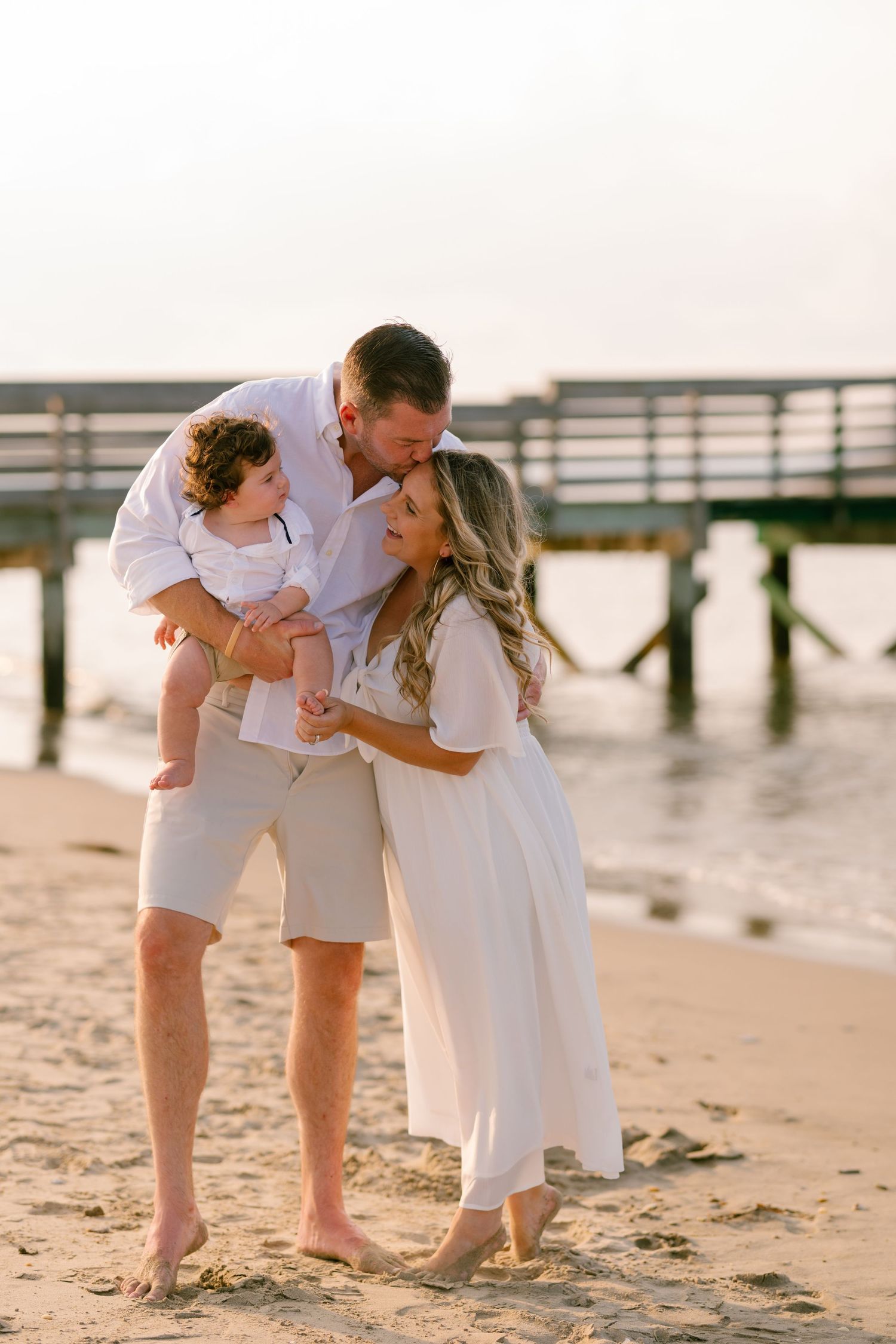 Family shares tender moment on beach at sunset near wooden pier.