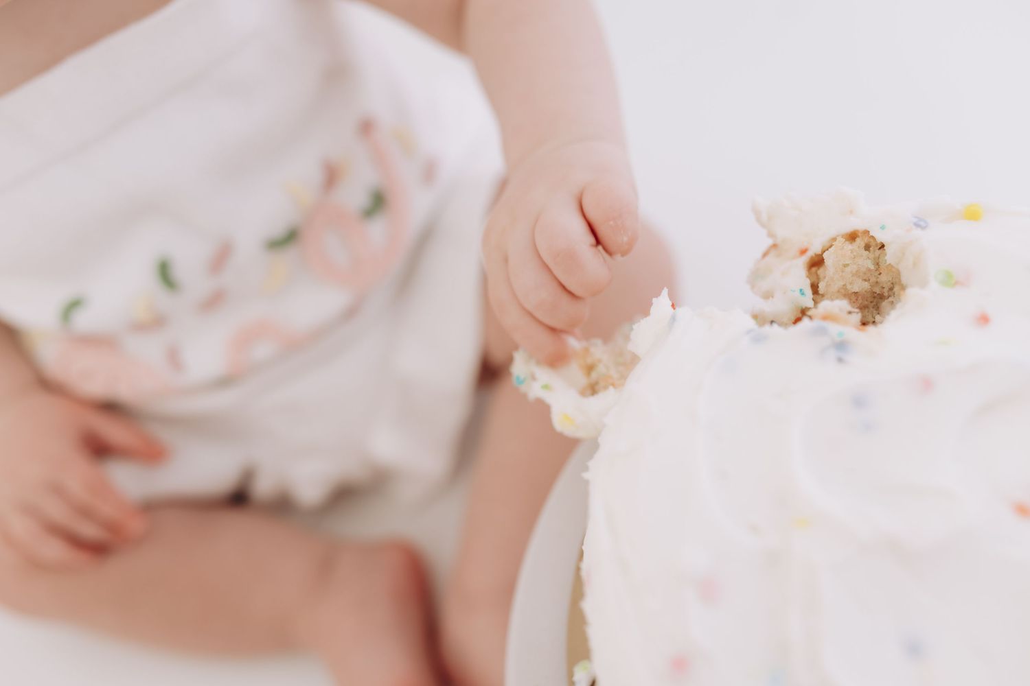 Close-up of small hands touching white frosted cake with sprinkles.