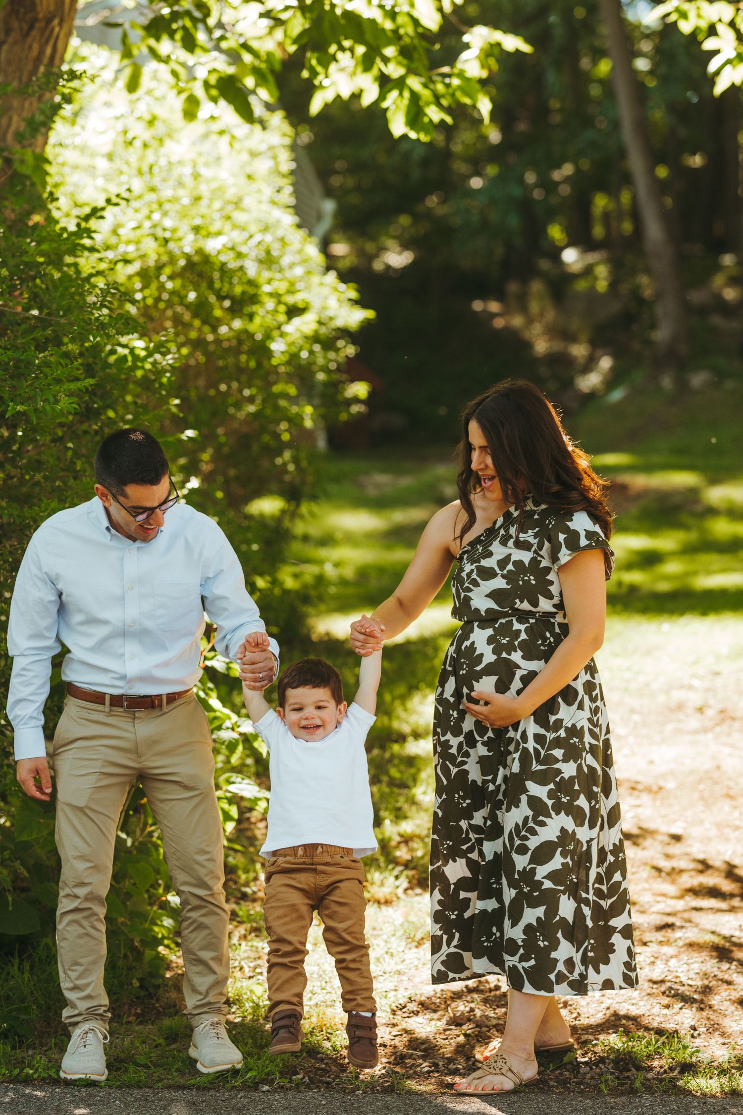 Family walking together on a tree-lined path while holding hands with their toddler.