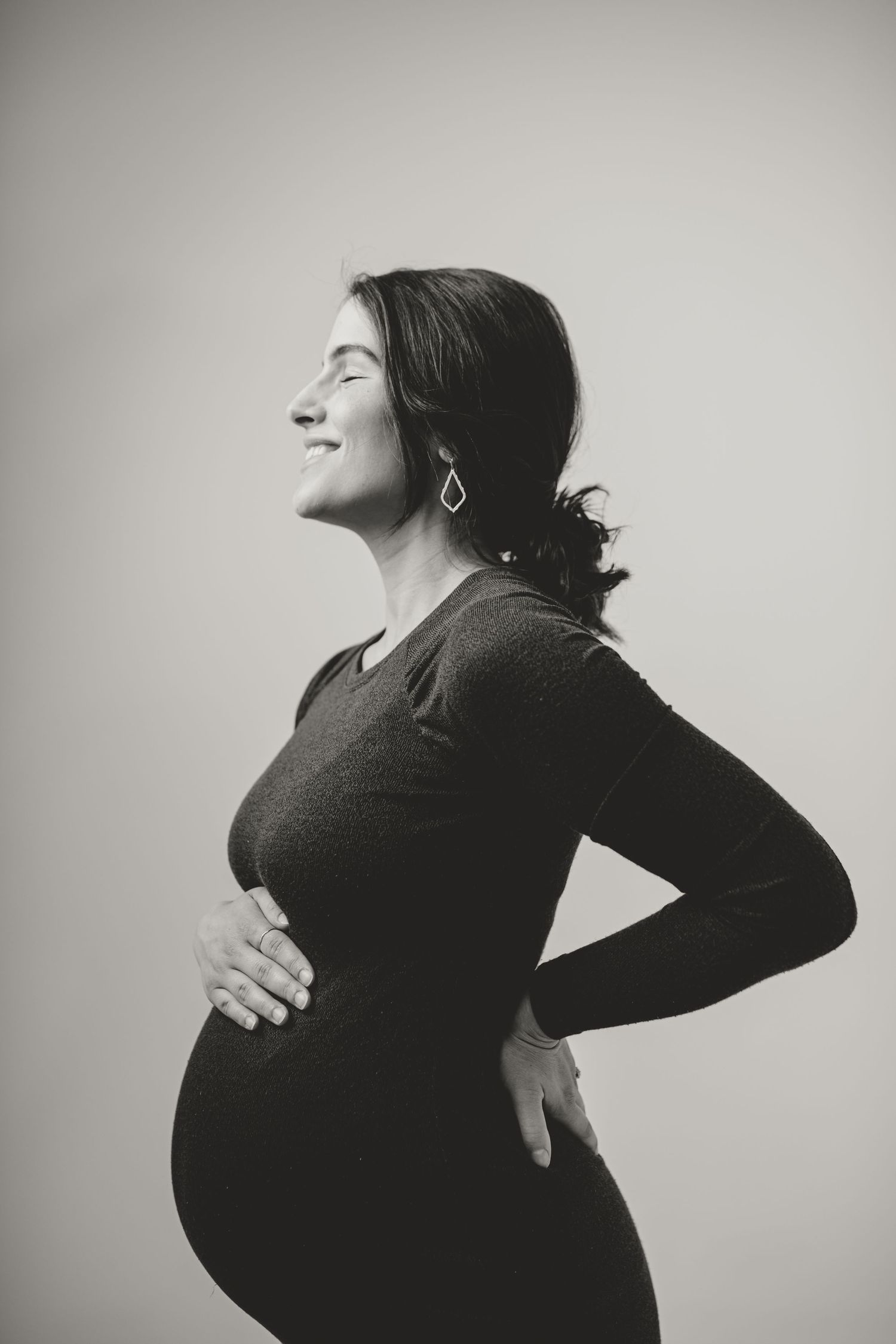 Black and white profile portrait of expectant mother in simple studio setting.