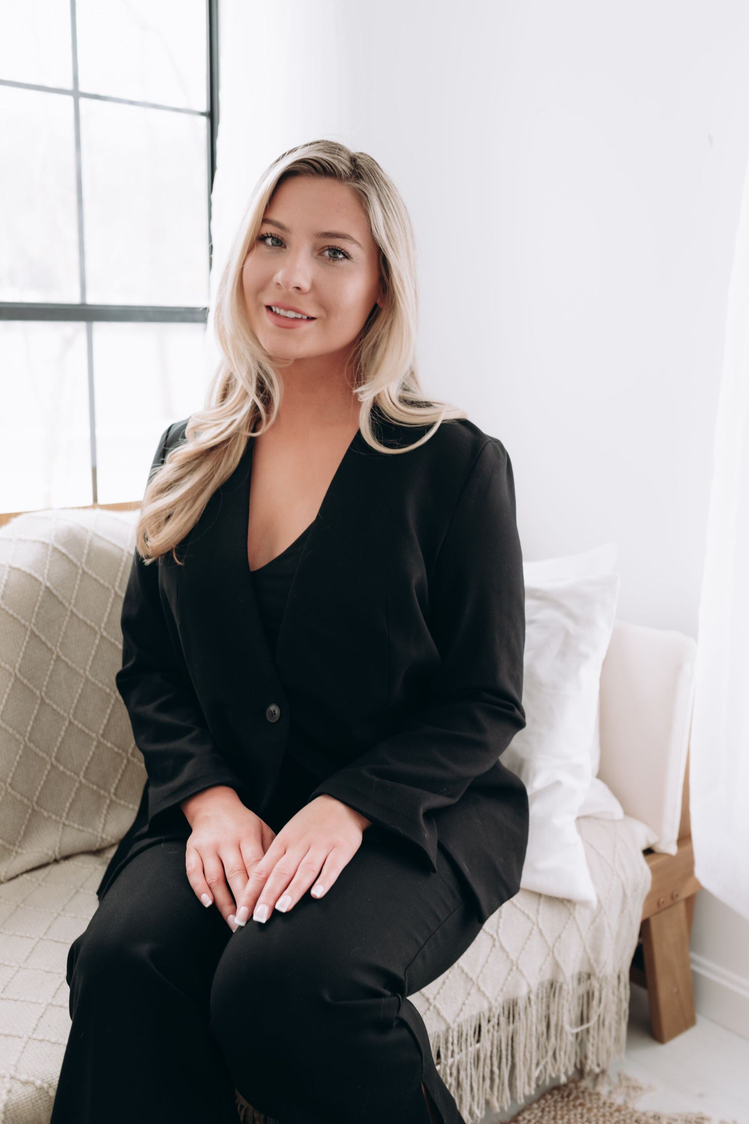 Professional photo session on couch wearing black outfit in bright setting.