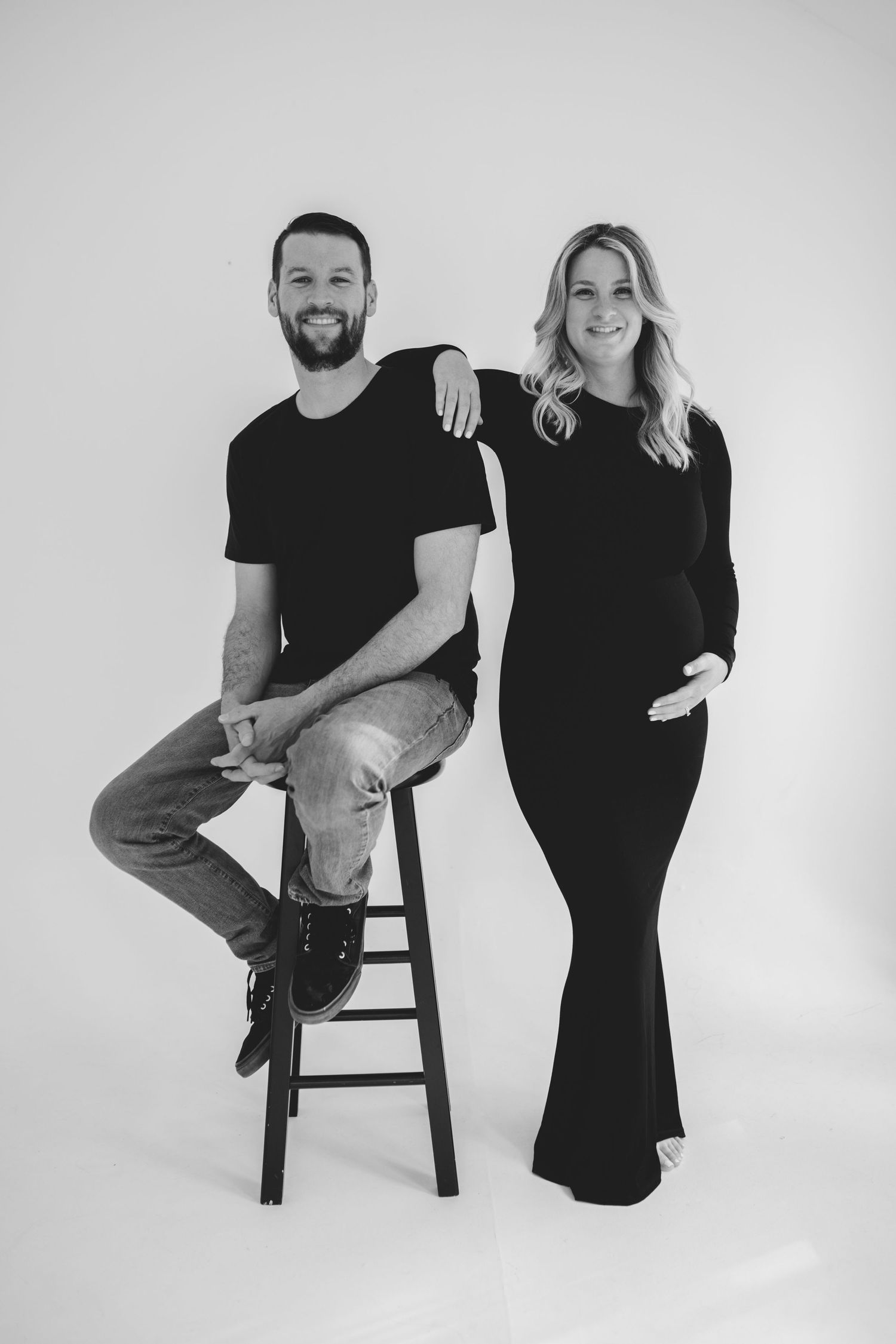 Black and white photo series showing a couple in minimal studio setting posed with a wooden stool against white backdrop.