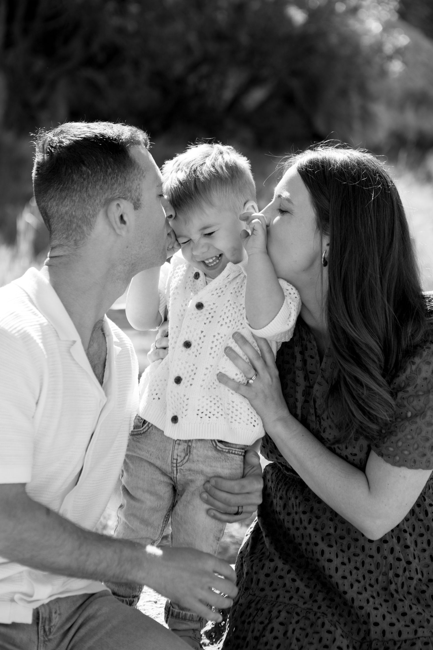 Sweet family moment captured in black and white as parents kiss their joyful young child.