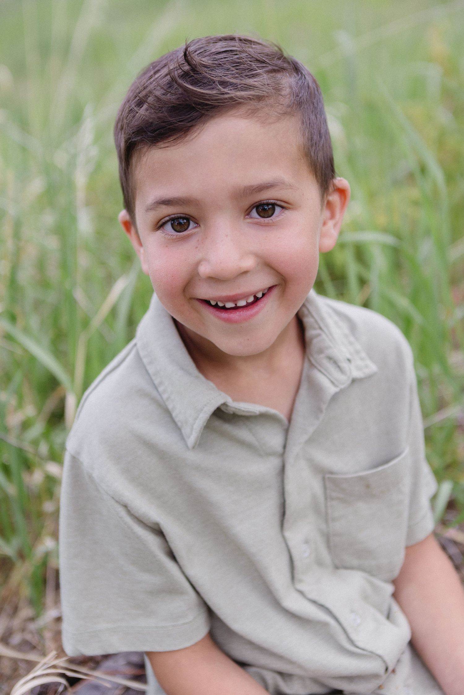 Candid portrait series of a young child in a gray shirt sitting in tall grass, showing different cheerful expressions.