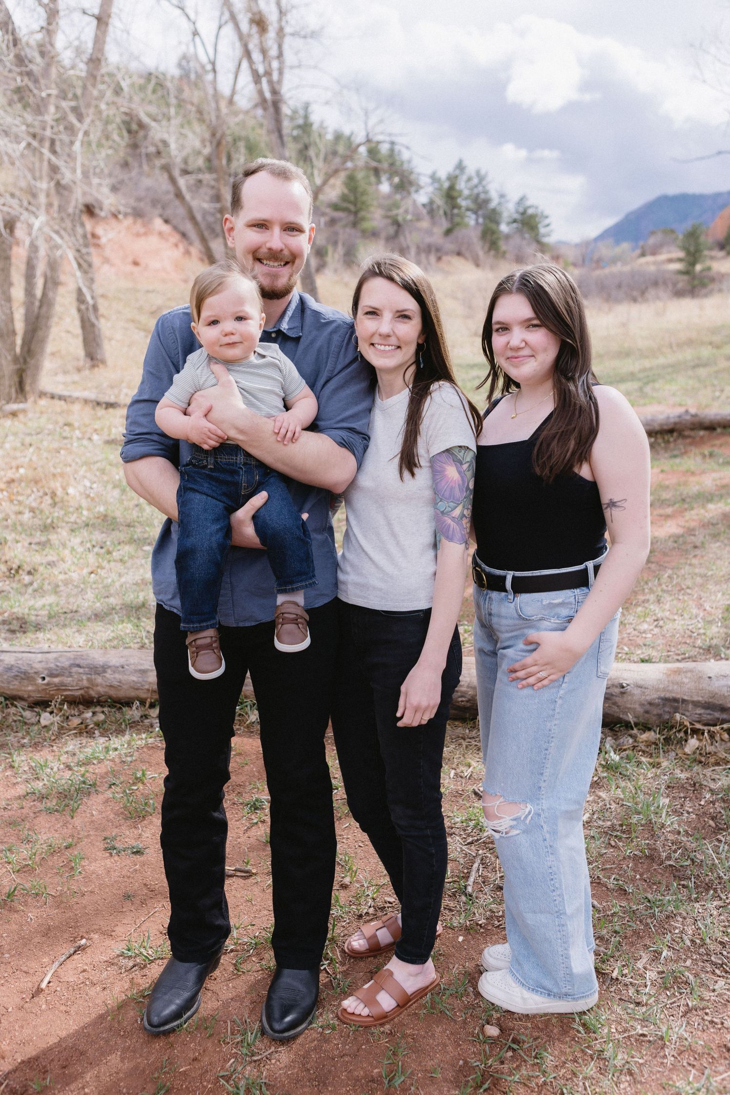 Family photo taken outdoors on a forested mountain trail during early spring.
