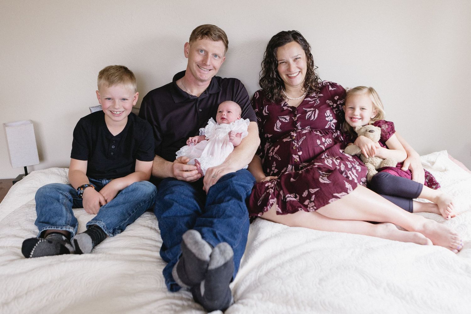 Family sitting together on white bed in casual clothing for indoor portrait session.