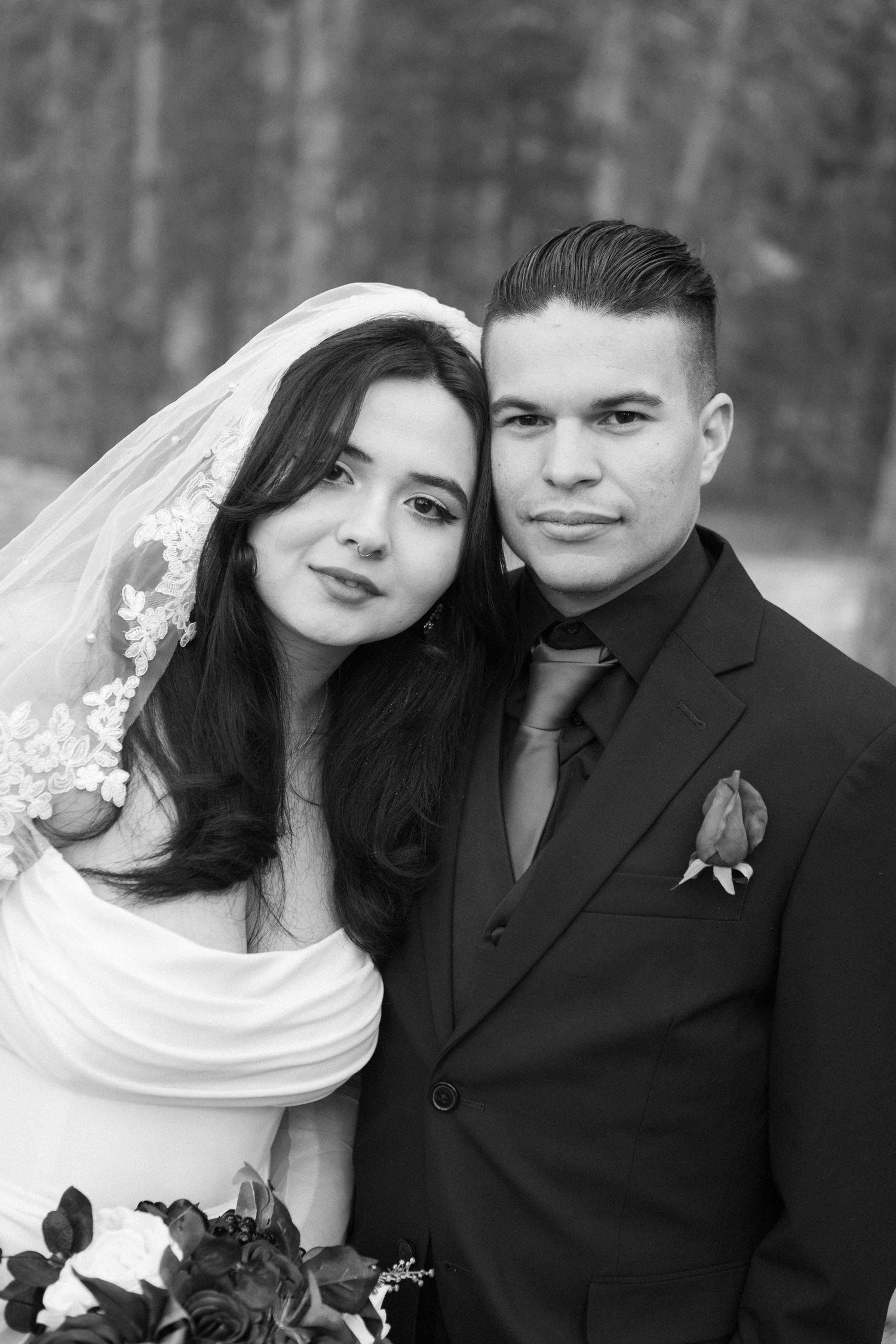 Black and white wedding portrait showing couple in traditional attire with bride in veil and groom in dark suit.