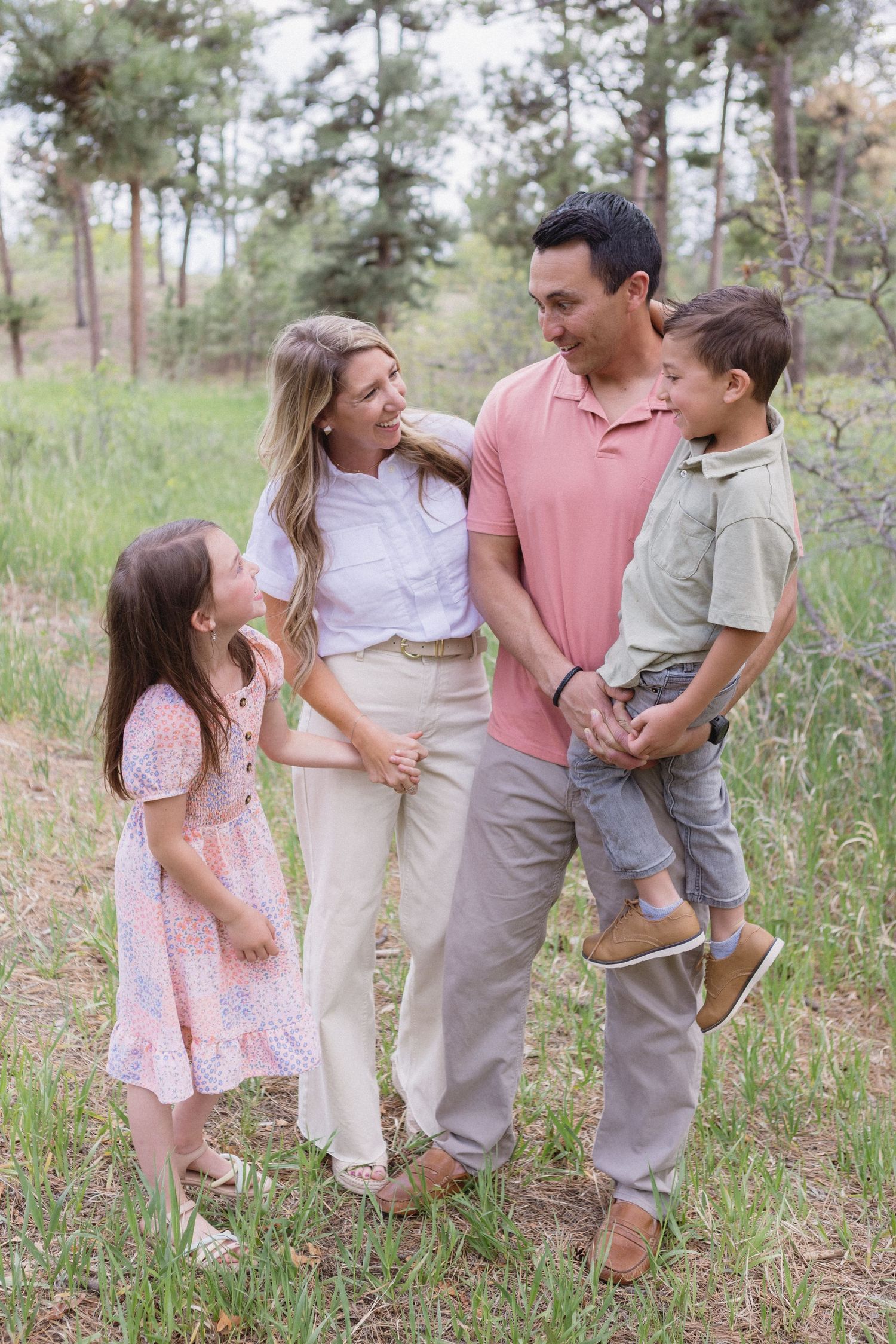 A happy family of four enjoying a candid moment together outdoors in a wooded natural setting.